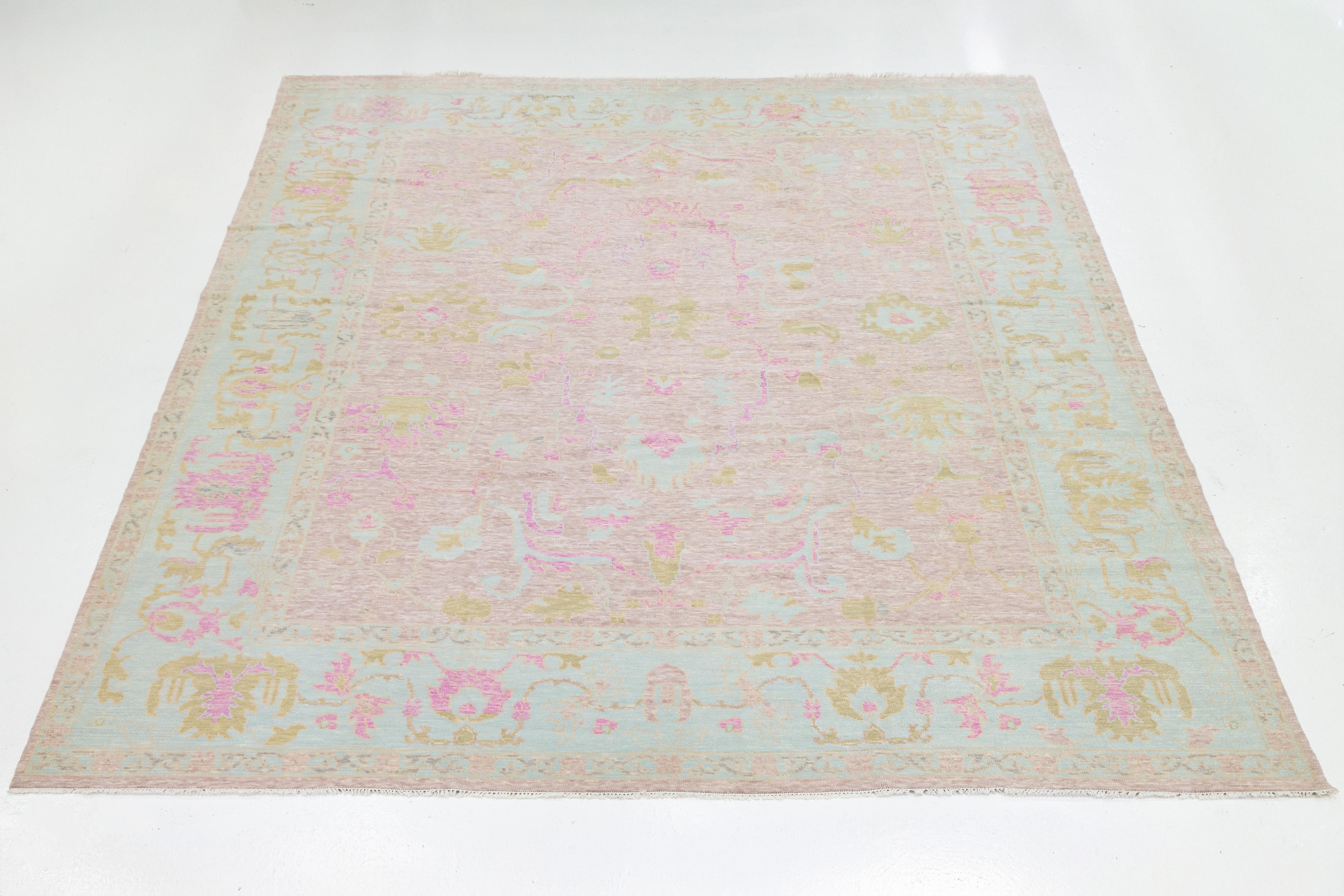 Dieser moderne Teppich im Oushak-Stil ist aus 100% Wolle handgeknüpft und zeigt ein raffiniertes Medaillon-Design mit zarten Blumenmotiven in beruhigenden Pastelltönen. Der subtile Schrägstrich und die vom Vintage-Stil inspirierte Farbpalette