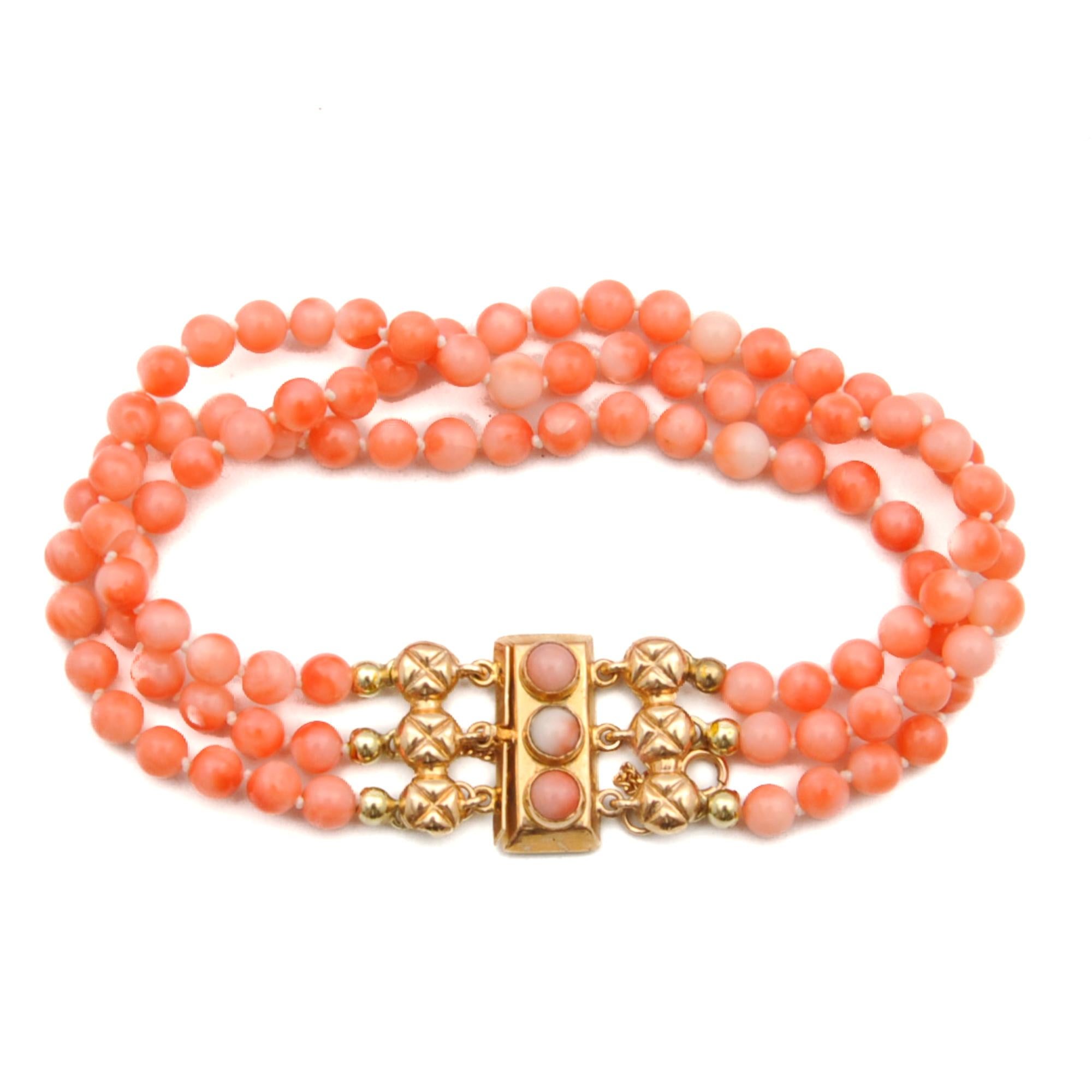 A 1920's Art Deco natural pink coral 14 karat gold three-strand beaded bracelet. The coral beads of this bracelet are round-shaped and are beautifully mottled with different hues of red and pink. The rectangular gold clasp is set with a row of three