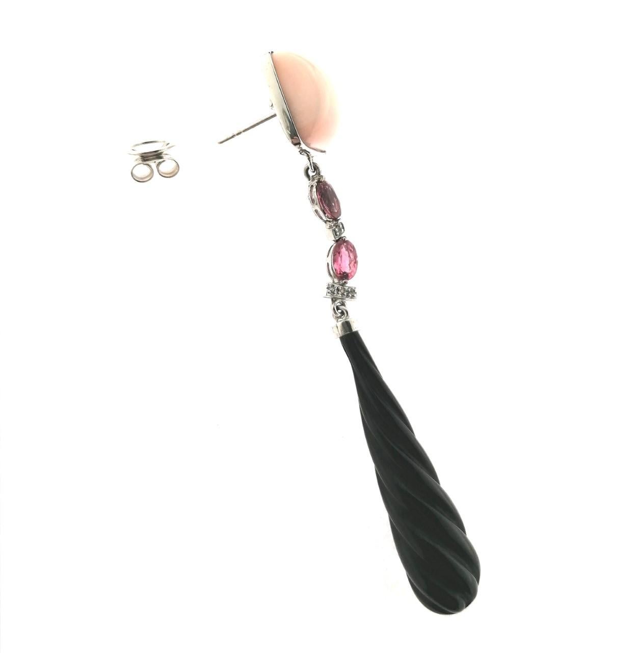Stylish 18 karat white gold with a cabochon of natural pink coral, two oval pink sapphires and brilliant cut diamonds in the upper part. Down, they have a carved long drop in onyx. Because of the lenght and its color, they are perfect for a female