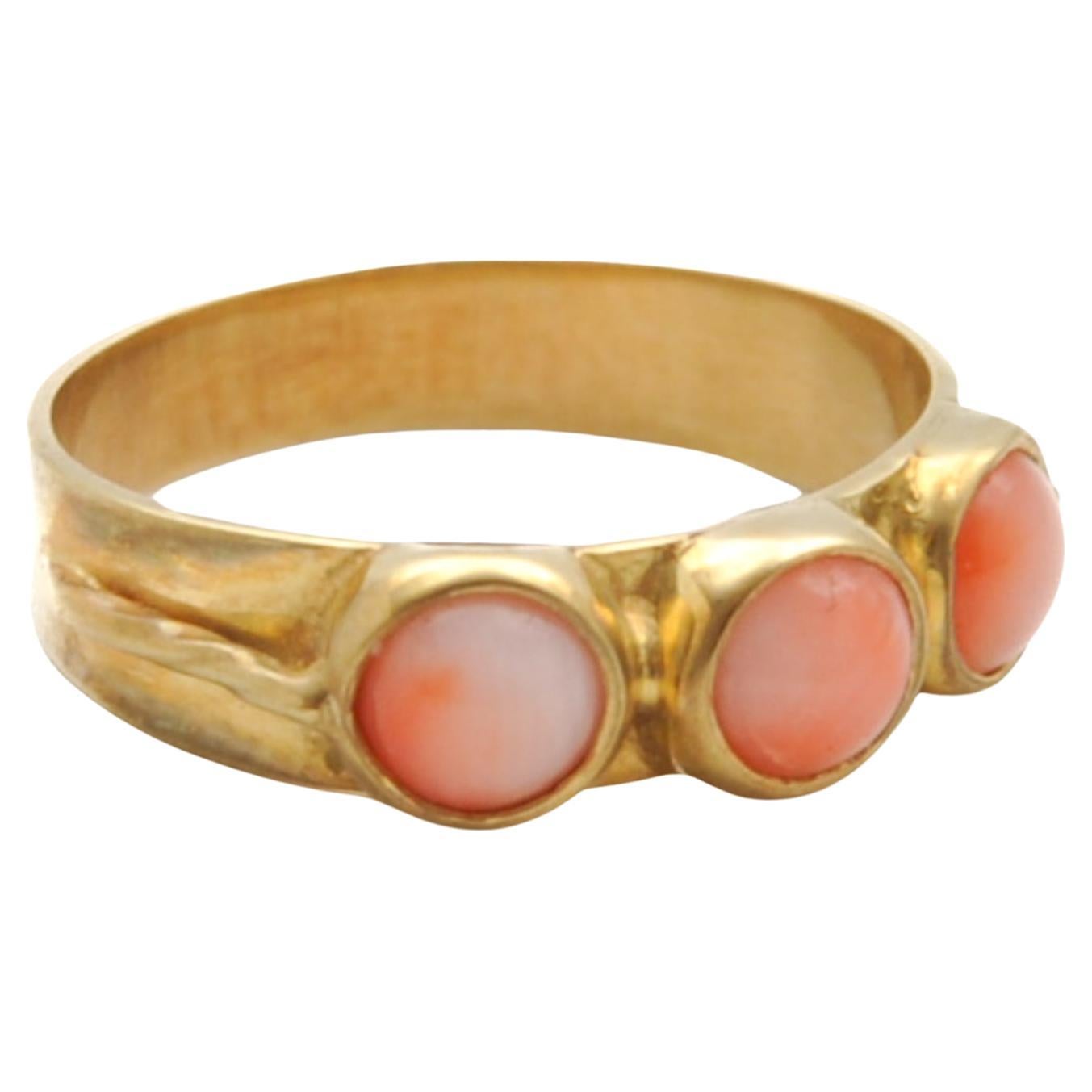 A vintage triple pink coral stone set in a gold band ring. The three stones are round shaped cabochons surrounded by a 14 karat yellow gold frame and bezel set. Coral is considered a symbol of renewal, vitality and beauty. The ring contains the pink