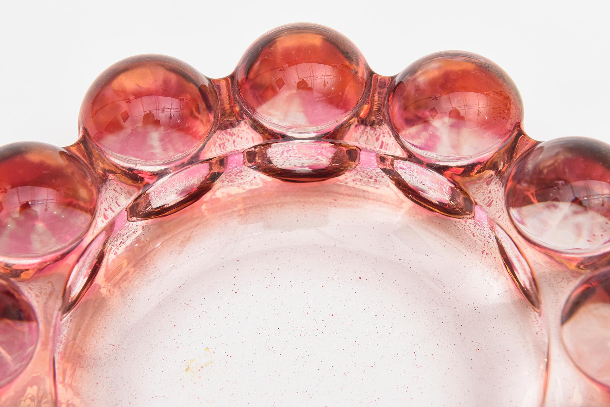 This ever so chic fun ring glass bowl has 12 round round semi dome balls as the exterior. It is American from the 40's. The colors are pink, hot pink and cranberry with clear glass. The colors change with the play of light. It is molded glass. Great