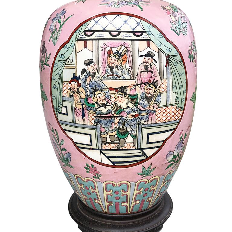 Pink famille rose chinoiserie Asian ginger jar turned lamp with accordion pleated shade. Piece features a pink background with hand painted floral arrangements throughout. (tulips, roses, marijuana leave and lotus flowers.) Front depicts a figural
