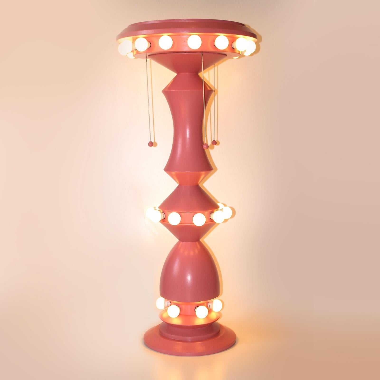 Evoking the shape of an old-fashion carousel, this table lamp by designer Mascia Meccani is handcrafted of lathe-turned wood with a geometric silhouette finished in vibrant pink. The top, middle and bottom rims feature 31 white lightbulbs in the