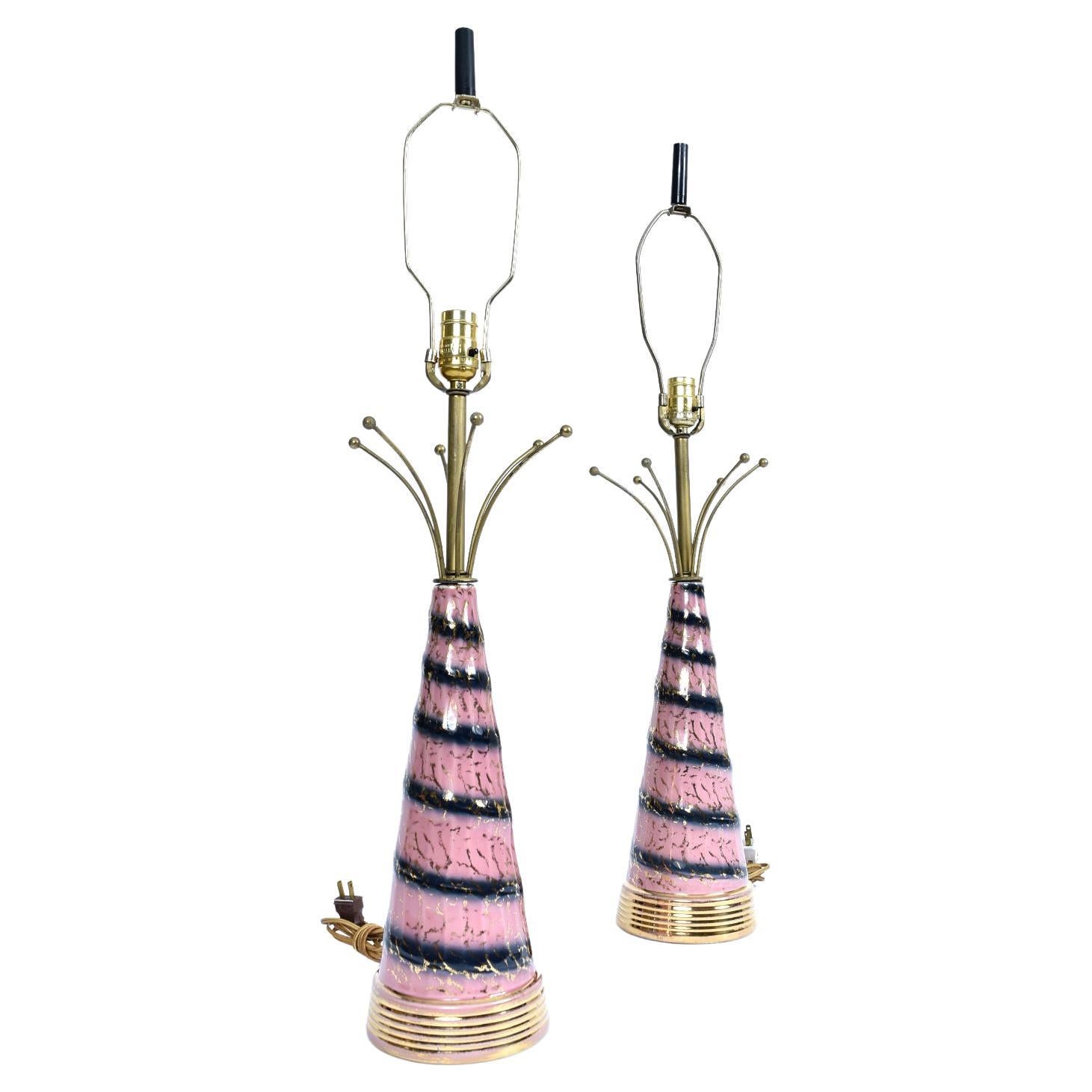 Delightfully novel pair of Mid-Century Modern atomic age lamps. The pink, gold and black lamps are topped with a whimsical “atomic age” metal embellishment. The gold colored steel spires are punctuated by gold spheres, a form inspired by the atom.