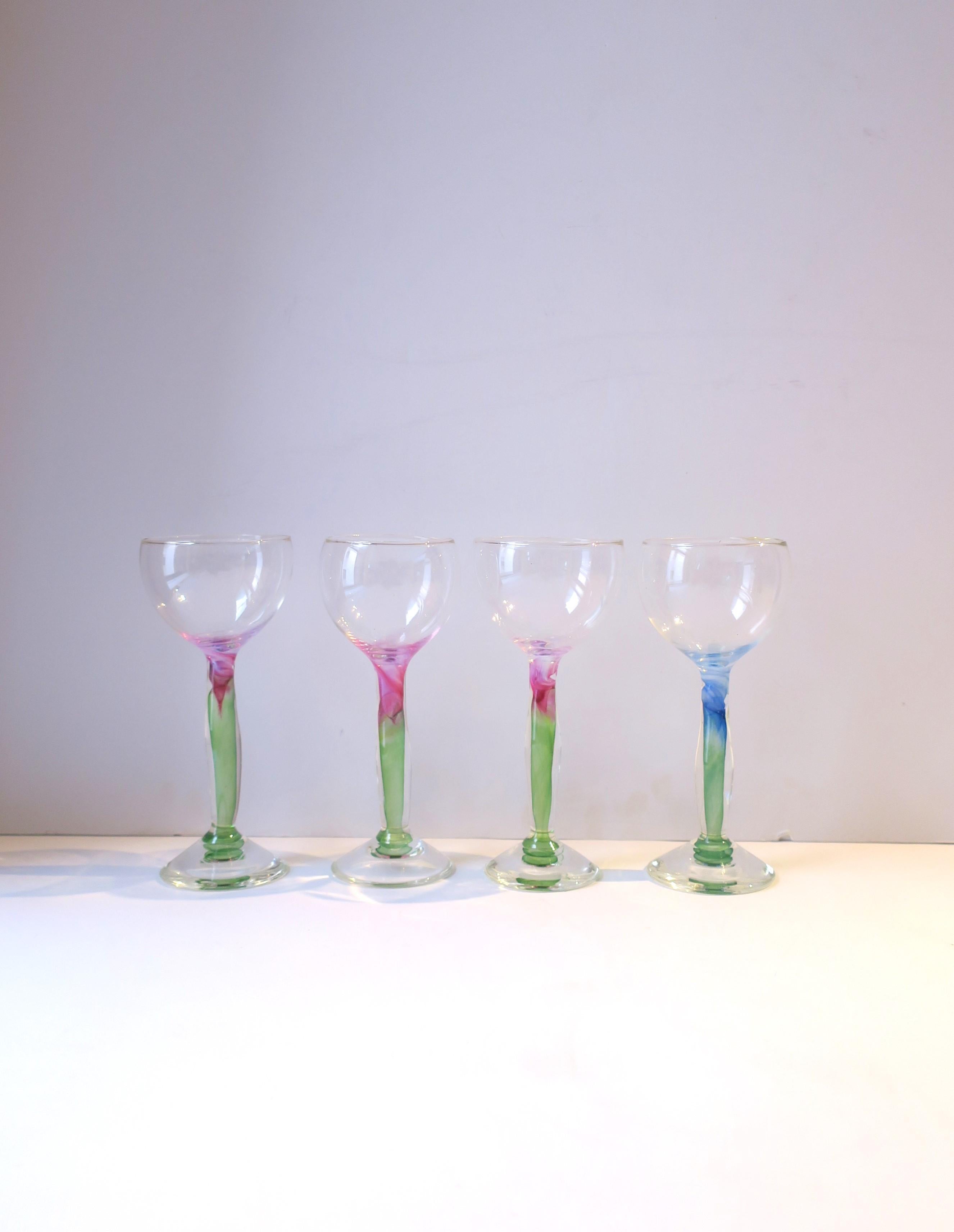 A beautiful set of four (4) water, wine, or cocktail glasses with an organic design, signed. Stems have an organic shape, three (3) with magenta pink and green art glass hues, and one with blue with green. All are signed on underside, closeup in