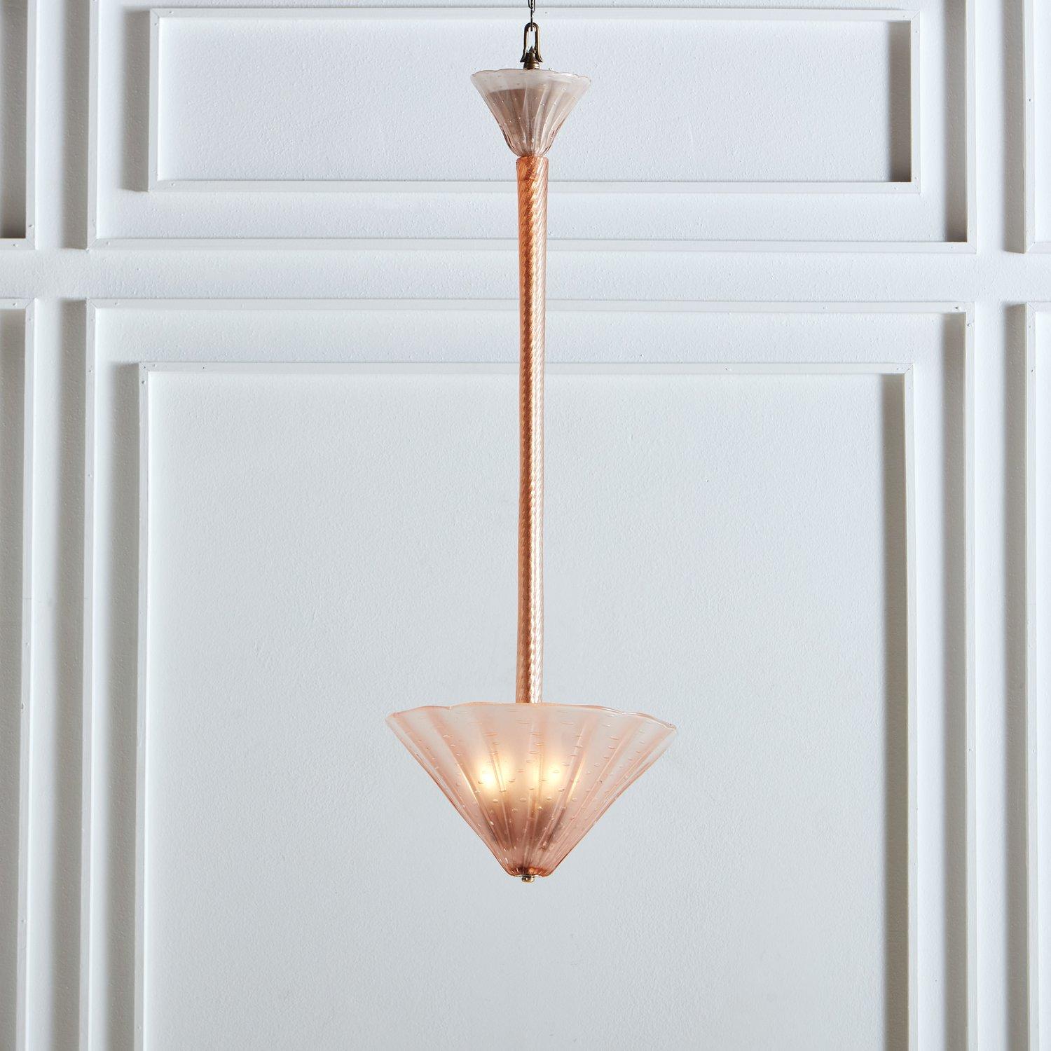 A gorgeous 1970s hand blown Murano glass pendant light. This elegant pendant has a pink fluted glass torchiere shade with subtle bubble details and a bottom chrome and brass finial. It hangs from a textured coral glass tube and has a pink glass
