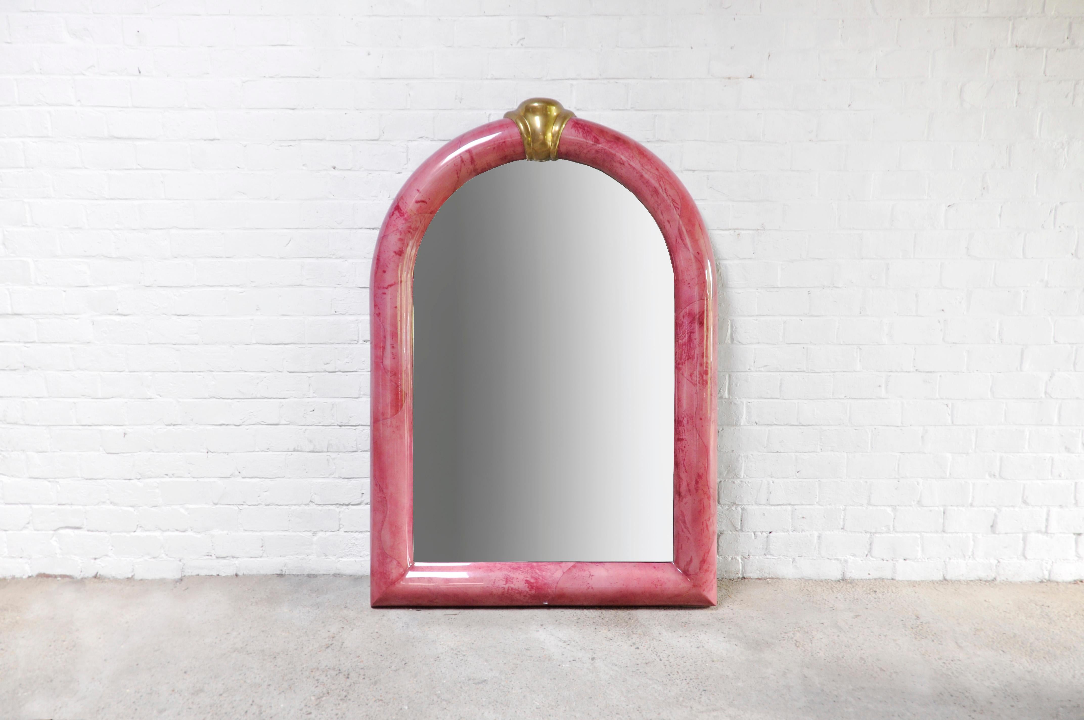 Monumental pink mirror by Karl Springer made in the 70s. The frame is constructed out of lacquered goatskin and is finished with a large brass accent on top. A very unusual and spectacular piece that will no doubt be the center of attention in any