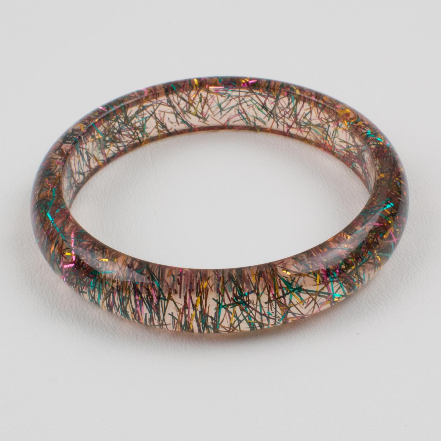 This lovely bangle bracelet has a domed shape and is made of transparent pinkish Lucite, injected with inclusions of metallic threads in multicolored tones. The metallic threads sparkle like those of Christmas tinsels. There is no visible maker's