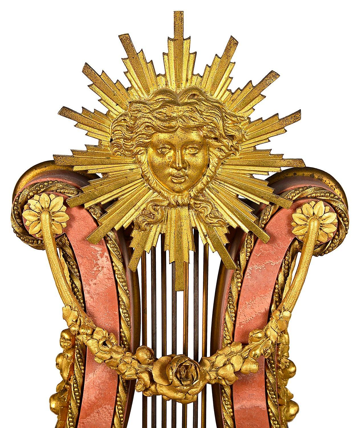 A good quality late 19th Century French Pink marble and gilded ormolu mounts, of a sun burst and swags above the Lyre. A white enamel clock face with an eight day duration movement that strikes on the hour and half hour. Riased on a stepped base