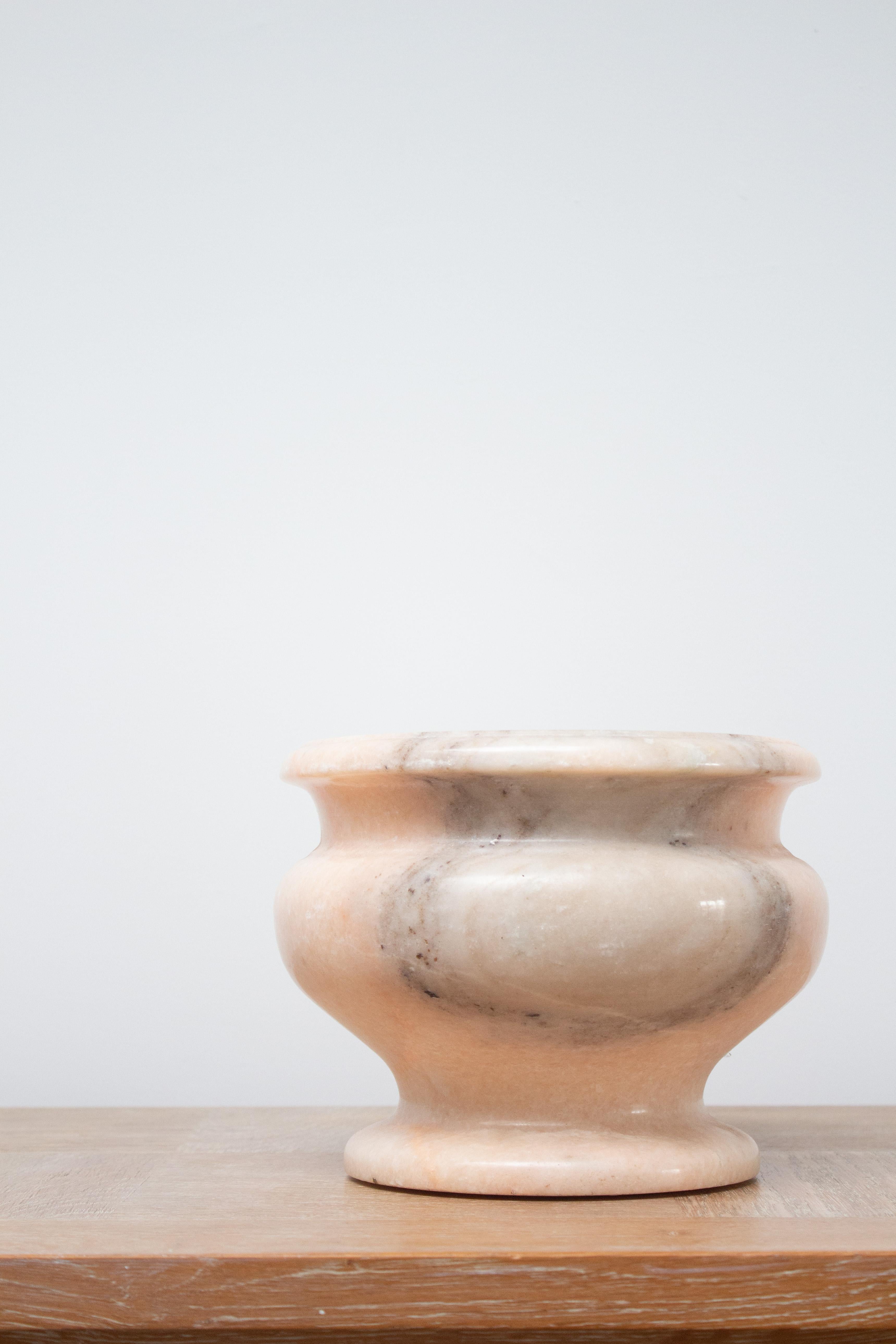 Un'urna in marmo rosa pallido. Le variazioni di colore vanno dal rosa al grigio chiaro e all'arancione. Finitura lucida. Silhouette classica di un'urna. Coppia disponibile, venduta singolarmente.