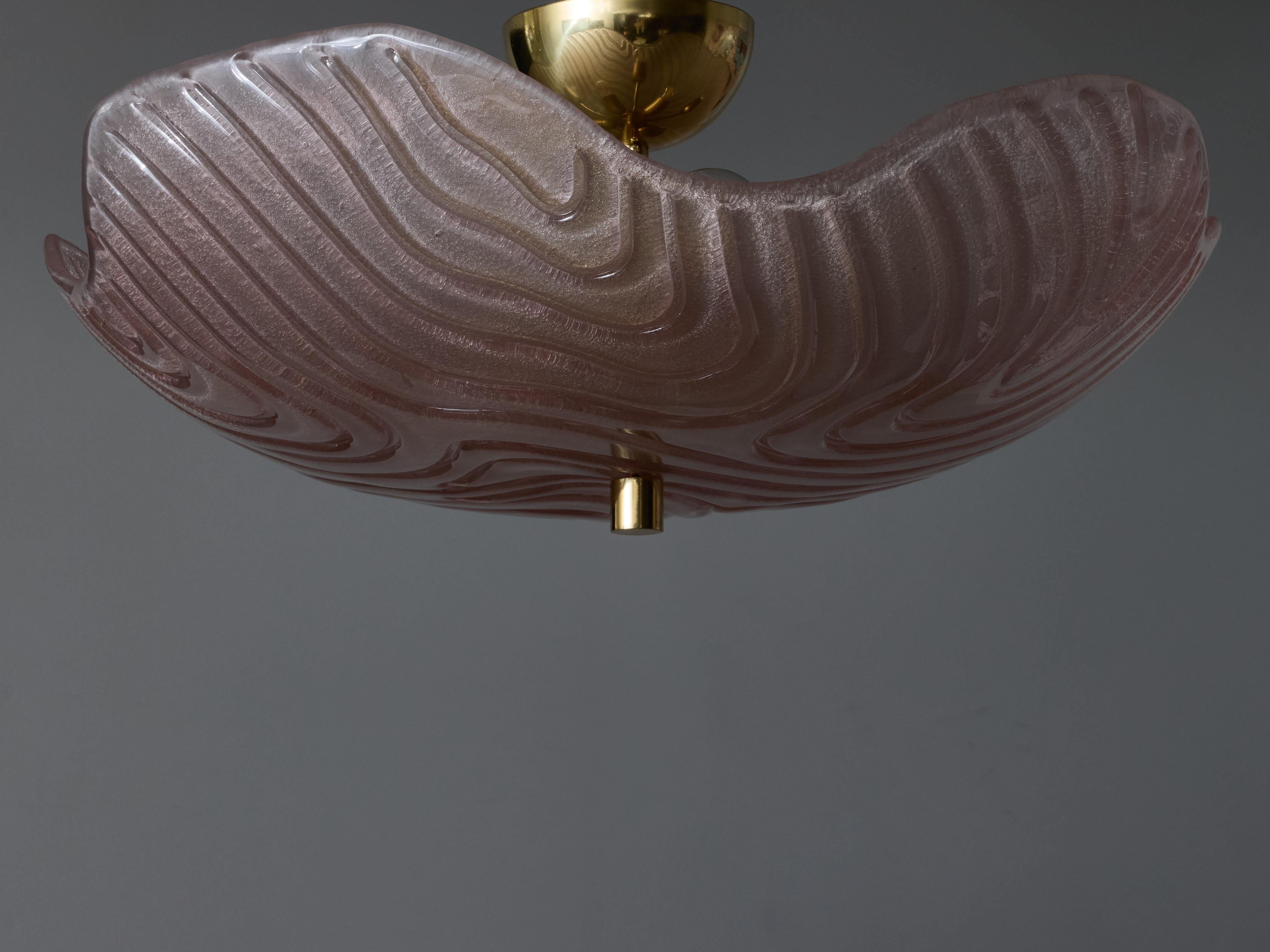 Montatura ad incasso composta da uno stelo in ottone che sorregge una ciotola in vetro di Murano rosa curvo e strutturato, che diffonde la luce delle lampadine ad altezza.