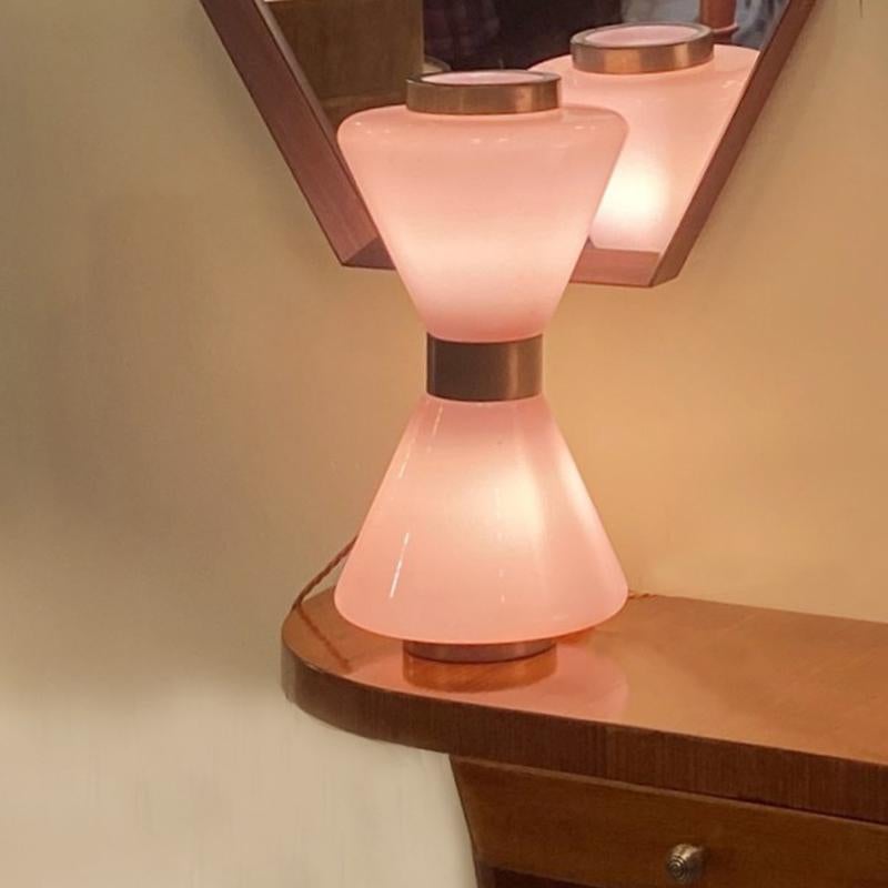Hourglass pink Murano 1950's table lamp in the style of Vistosi gives very atmospheric light. The glass is encased at the top, middle and bottom with brass colour metal. The Murano glass is blown in two layers, the inner white layer reflects the