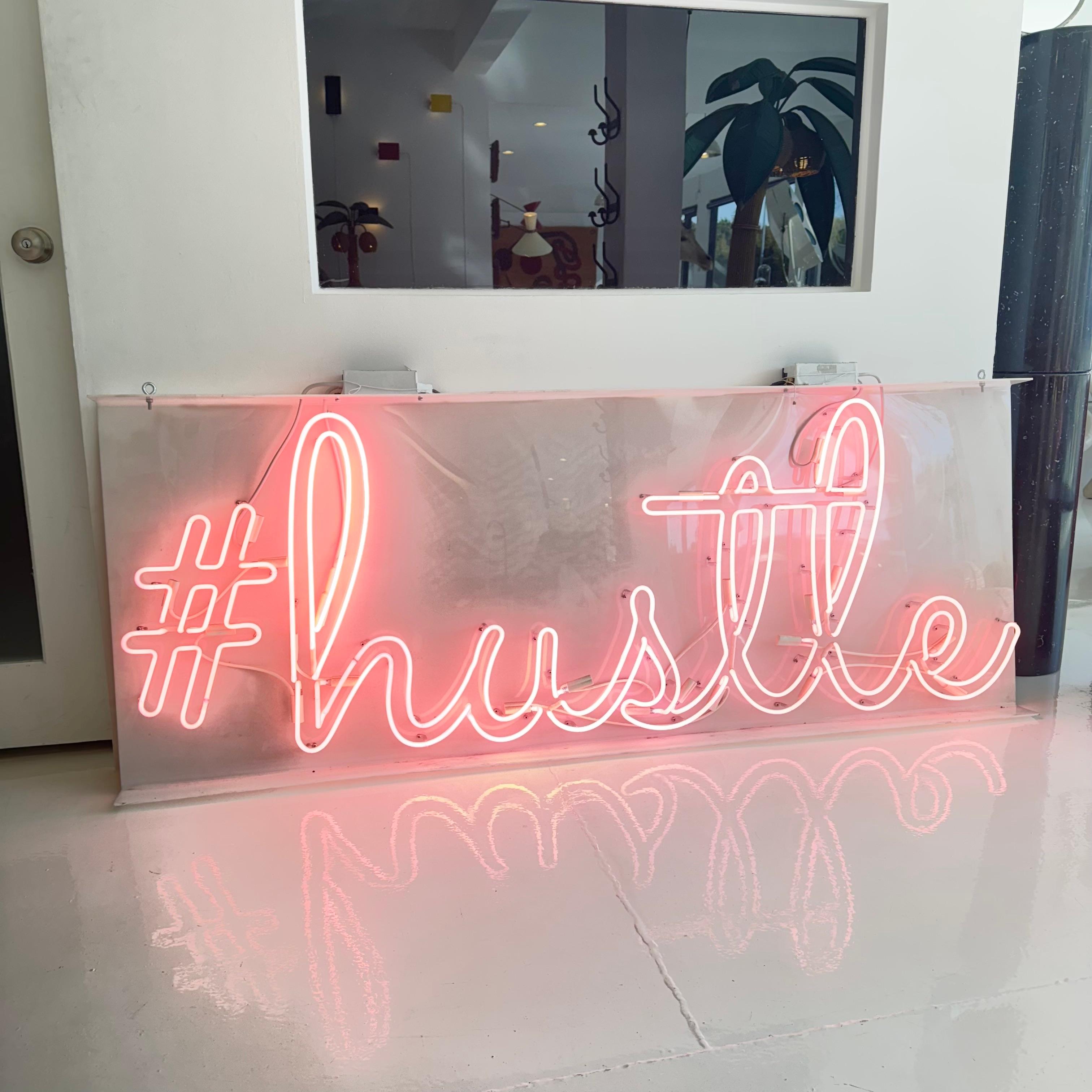 Massive pink neon sign mounted on white acrylic board. Sign depicts a large hashtag and the word hustle in cursive lettering. Light pink hue to neon. Great condition. Difference in coloring is simply the photo/lens. Color is a light pink
