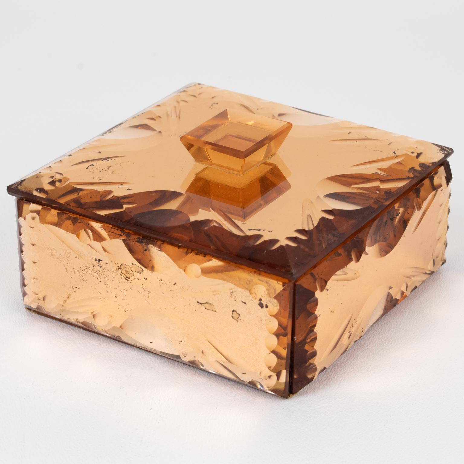 Esta preciosa caja decorativa de cristal espejado se fabricó en la década de 1940. El diseño cuadrado presenta un cristal de color melocotón rosado con un efecto de textura de espejo y un profundo biselado geométrico a su alrededor. El interior es