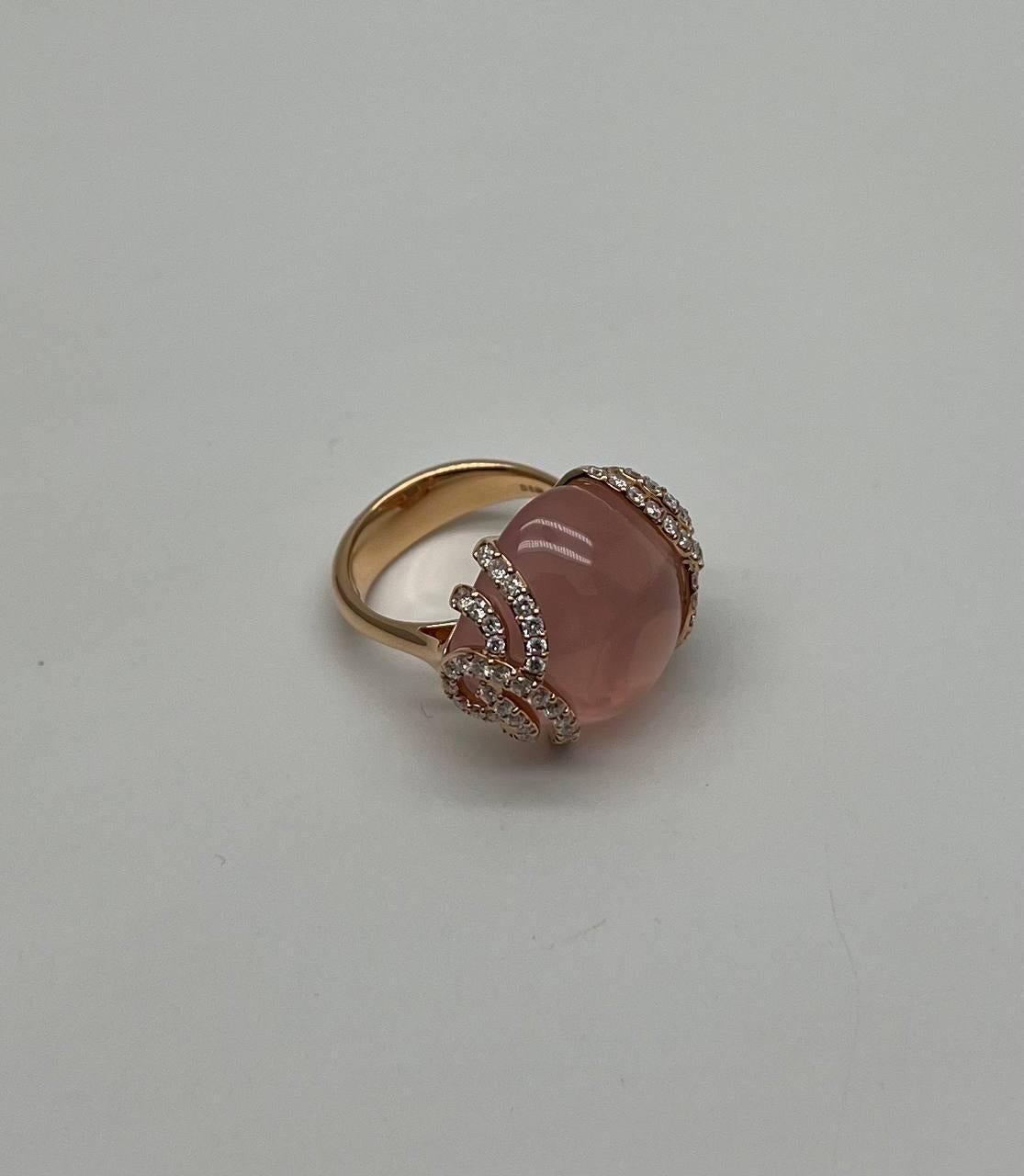 A fusion of elegance and modernity.
This striking ring features a captivating, smooth pink rose quartz stone. The central gem is embraced by intricate, diamond-studded bands that add a touch of sparkle and sophistication. The warm gold setting