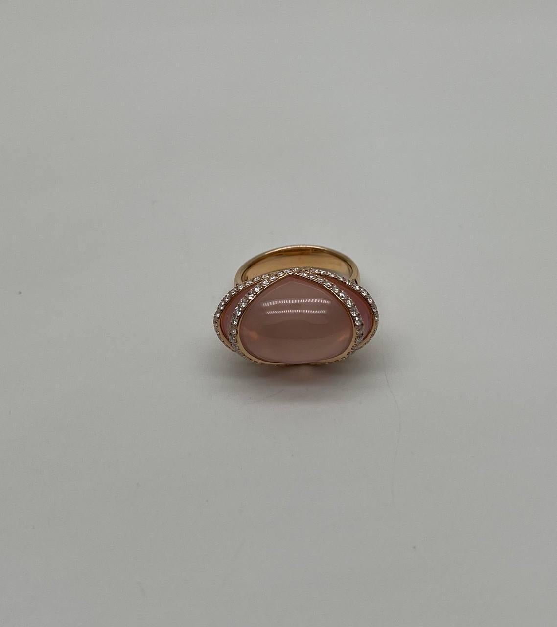 A stunning ring. This exquisite piece features a captivating design. The ring showcases a large, smooth cabochon rose quartz with a soft, translucent pink hue. It is elegantly framed by a halo of sparkling diamonds, adding a touch of brilliance to