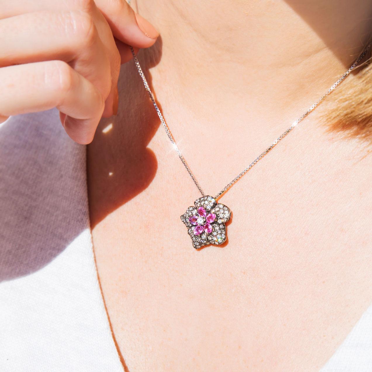 Carefully crafted in 18 carat white gold, and black rhodium plated, is this unique vintage flower cluster slider pendant.  Featuring a single round brilliant cut diamond surrounded by five pear shaped bright pink sapphires and embellished with a