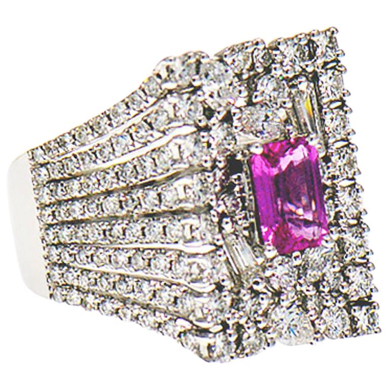 This gorgeous ring is a real show stopper. Featuring a rich pleasant emerald cut 1.00 ct. pink sapphire center set in four prongs on a platform of multi-shape diamonds. This is a large ring with a very unique design. The rectangular shape of the