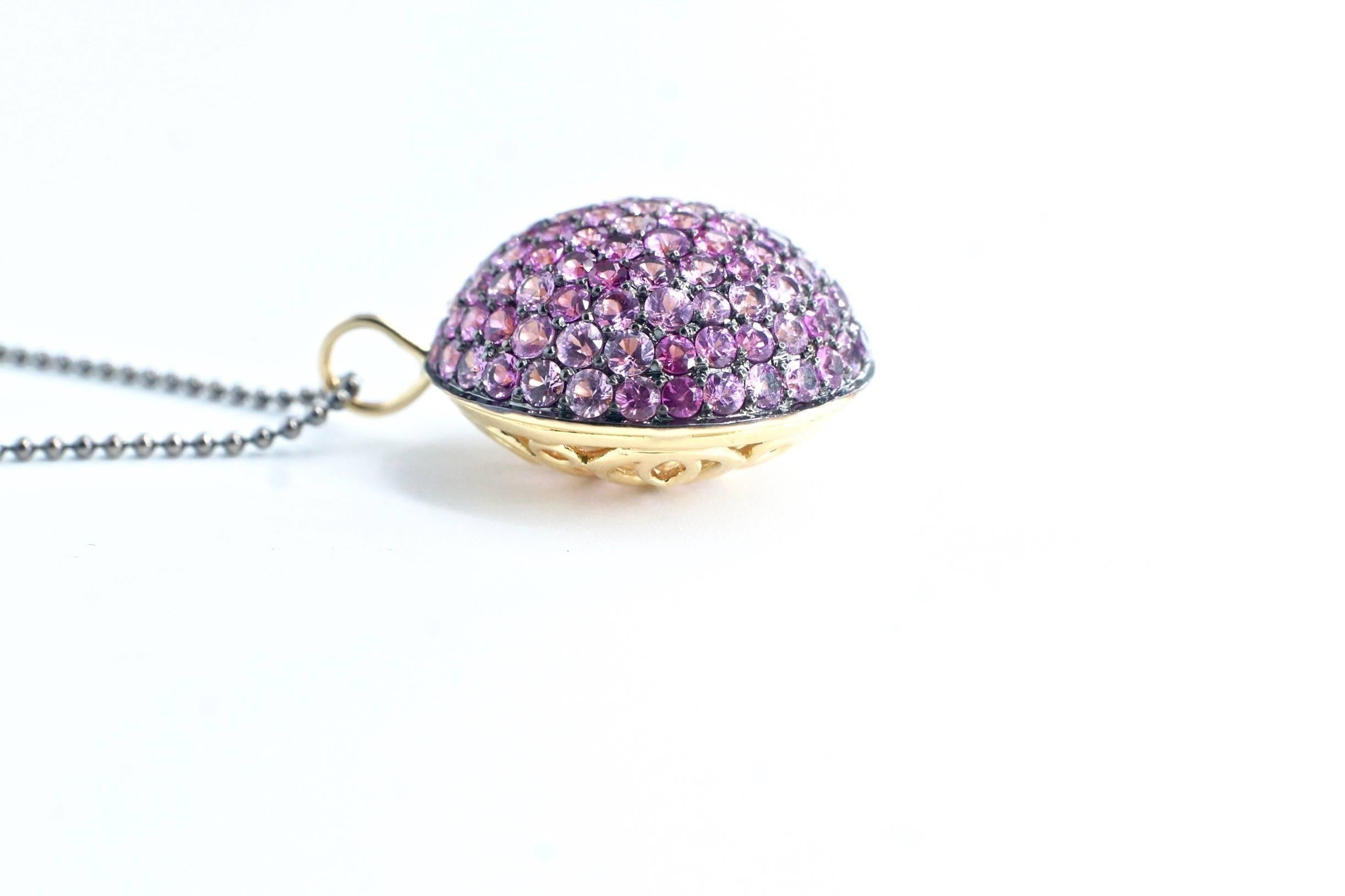 Pink Sapphire Lentil Pendant
A thirty-one-inch blackened white gold bead chain suspending a single eighteen-karat yellow gold pendant. The bombe pendant is set completely with pink sapphires on one side, while the verso consists of intricately