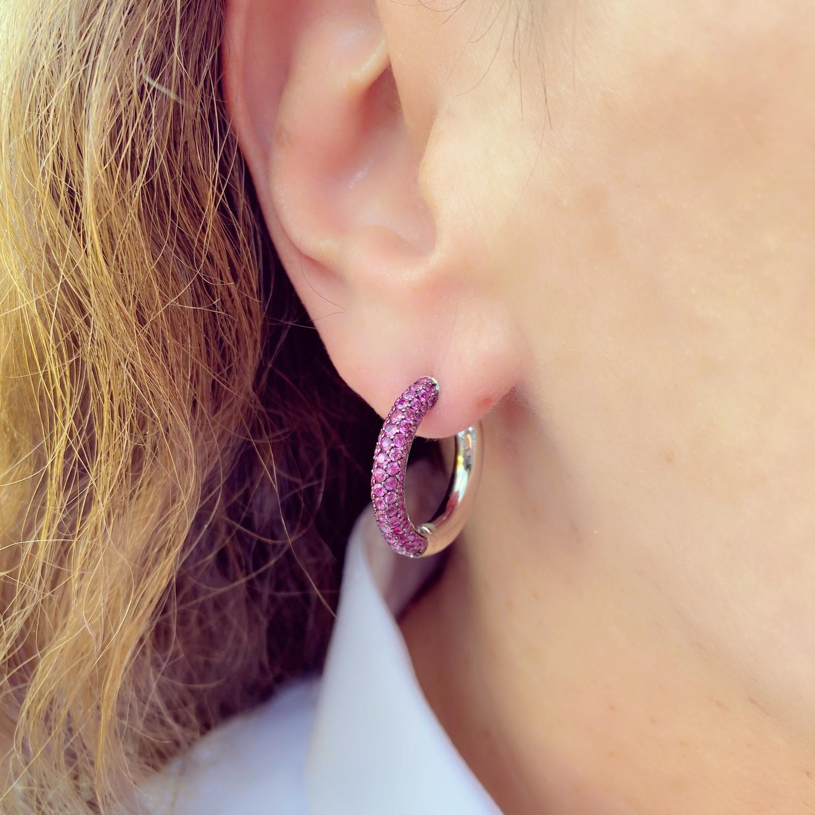 For the lover of all things pink! A fun version of a classic hoop design, these 18k white gold earrings are pave-set with 98 round pink sapphires, weighing in total 1.14 carats, They weigh 9.2 grams and measure 7/8 inches long. Unique and fun!