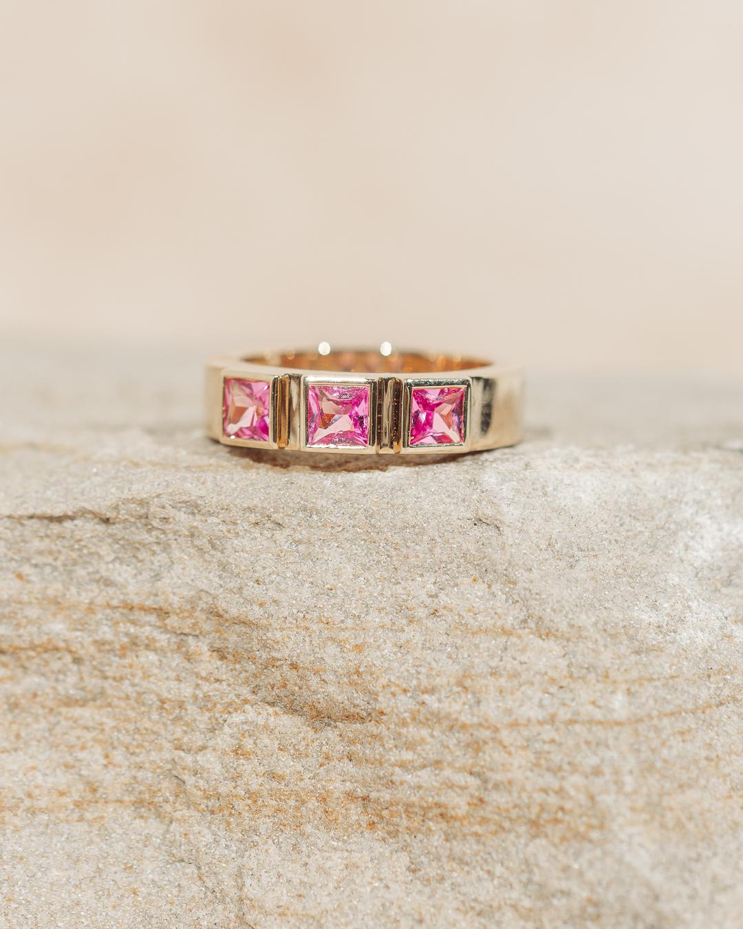 Setzen Sie ein kühnes, aber elegantes Statement mit diesem atemberaubenden, fein gearbeiteten 3-Stein-Ring aus rosa Saphir. 3 große Saphire im Prinzess-Schliff entsprechen 1,215 ctw und sind in 14k Gelbgold eingefasst. Die Nachfrage nach rosa