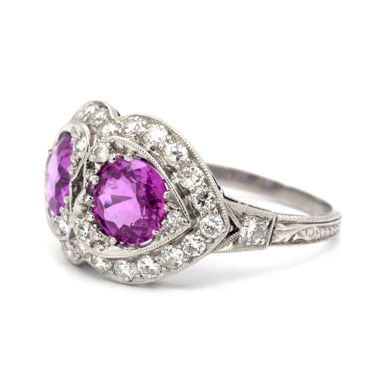 This Pink Sapphire and Diamond, Art Deco style, 18k white gold ring features two round Pink Sapphires. Each one measures 6.5 mm and have a total weight of 2.45 cts. These pink sapphires are beautifully offset by 32 rbc clean white diamonds that