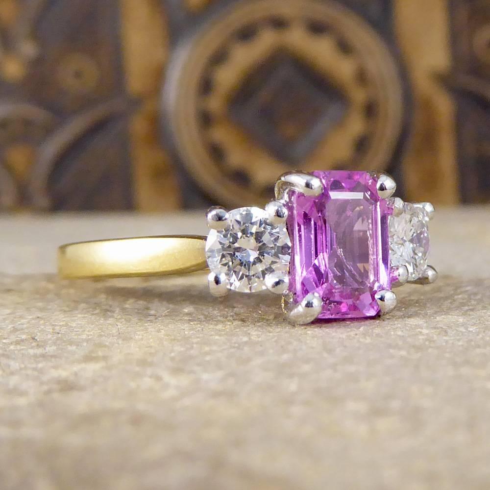 This classic and bold three stone ring holds one dazzling claw set emerald cut Pink Sapphire weighing 1.00ct, flanked on either side by a total of two Diamonds weighing 0.25ct each. This contemporary ring is crafted with a yellow Gold band leading
