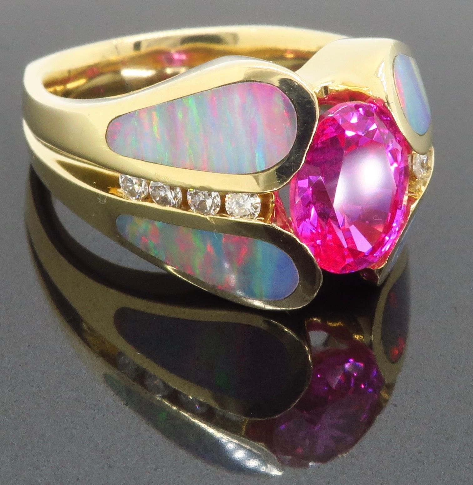 Custom Pink Sapphire, Opal, and Diamond ring made in 14k yellow gold.

Center Gemstone: Pink Sapphire 
Center Gemstone size: 8.09mm x 6.24mm 
Diamond Carat Weight: Approximately .20CTW 
Diamond Cut: Round Brilliant Cut
Metal:  14k
Marked/Tested: