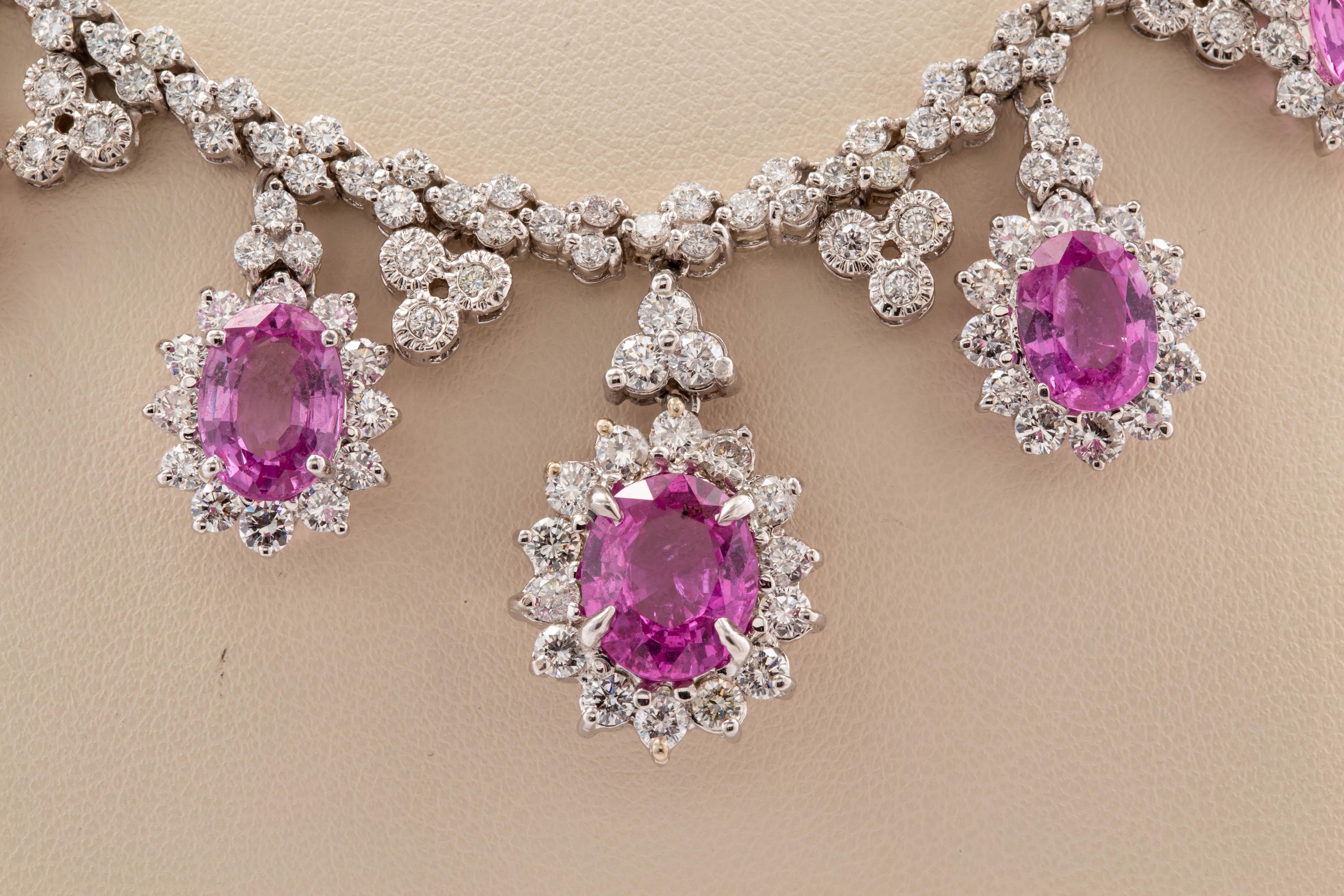 18 karat white gold custom made Pink sapphire and diamond cluster necklace, consisting of 13 oval cut Pink sapphires, with a total carat weigh of 24.60 carats, surrounded by round brilliant cut diamonds all prong set and dangling from a 16 inch