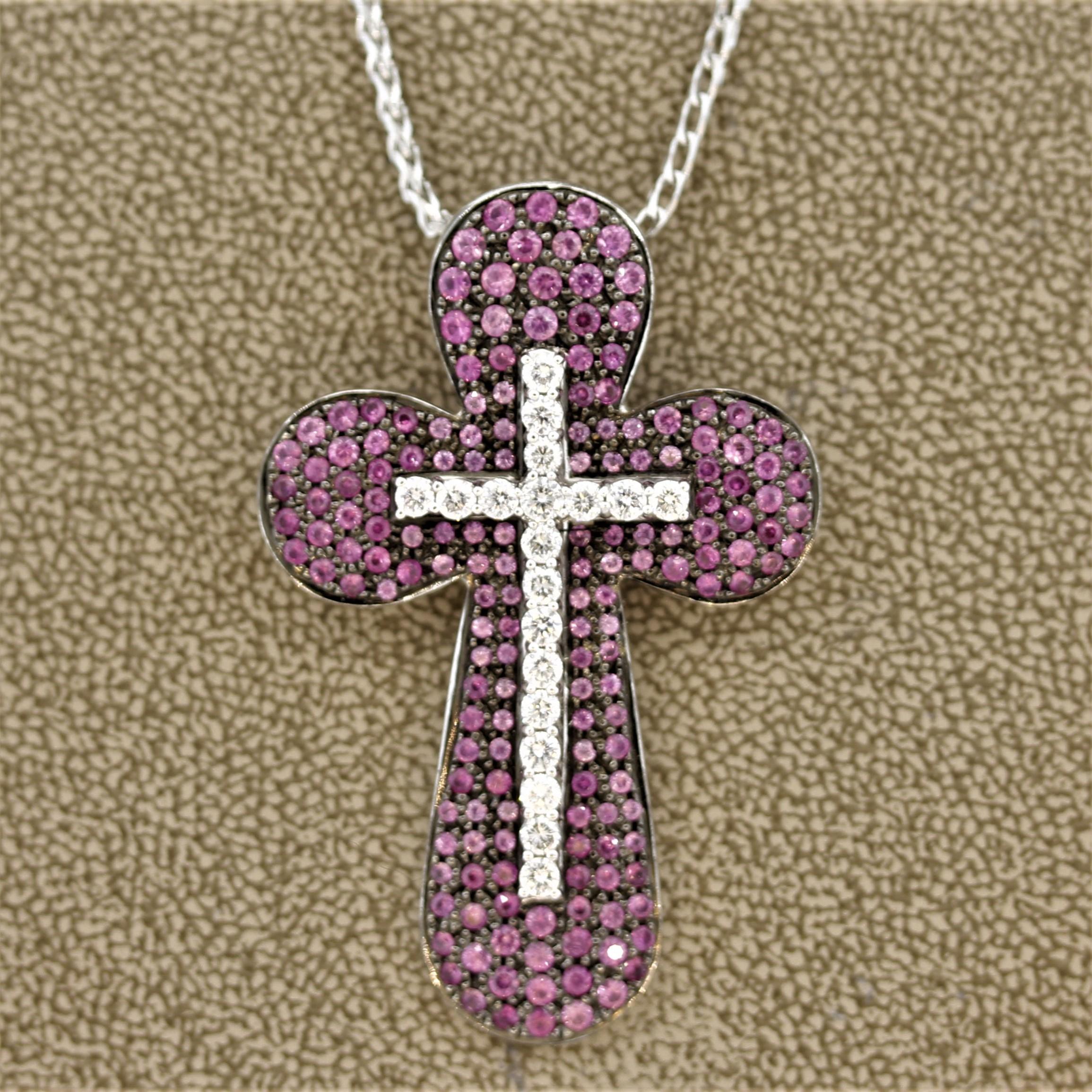 A large and unique cross pendant. It features a rounded cross set with 2.67 carats of pink sapphires in various shades, which has another cross set atop it. The second cross is set with 0.90 carats of round brilliant cut diamonds. Made in 18k white