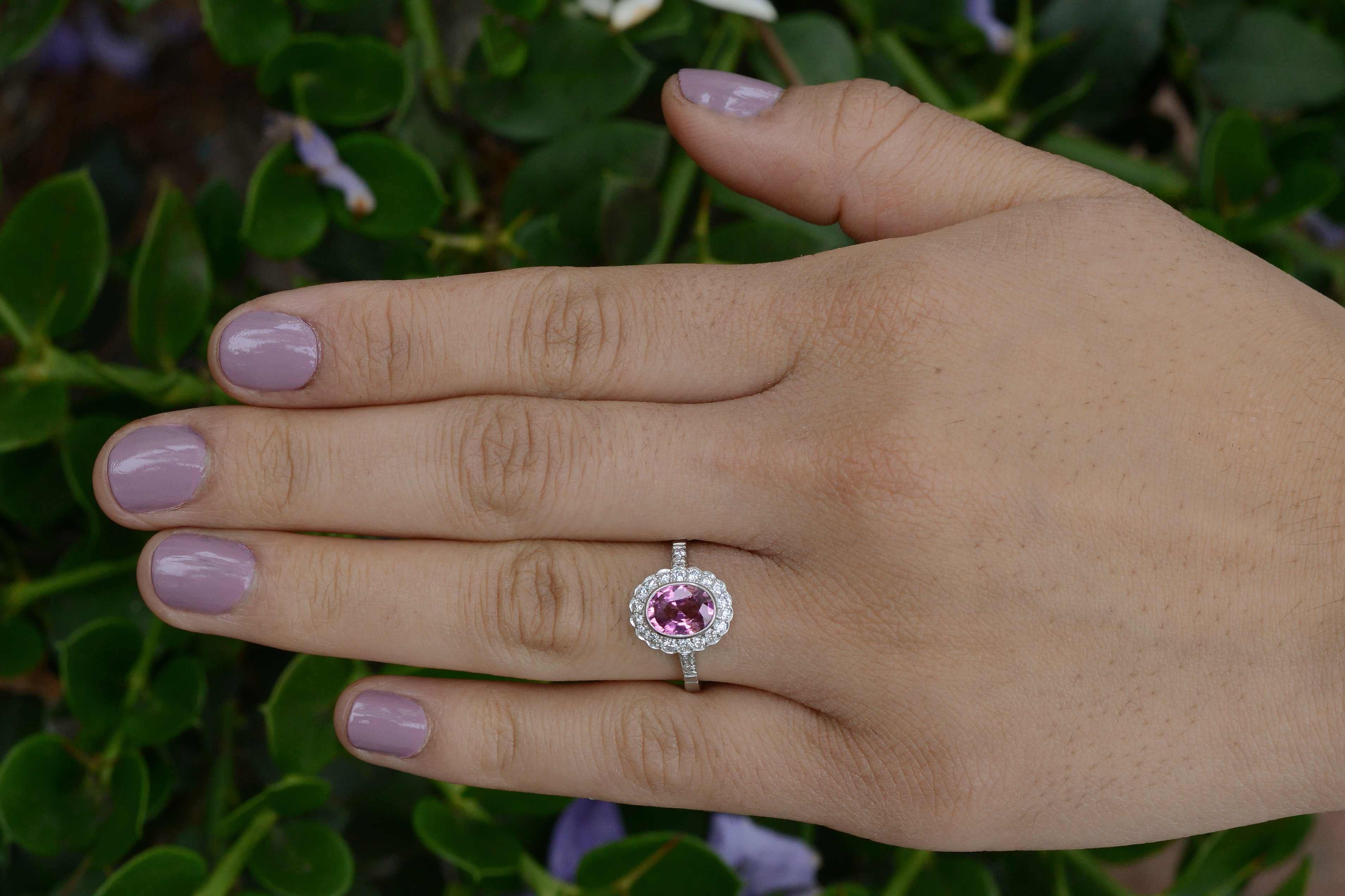 This dynamic and vivid pink sapphire engagement ring boasts a sizable 1 1/2 carat, eye-popping natural gemstone at it's center and is caressed by an angelic oval halo of 24 glimmering, brilliant round diamonds. The Art Deco Style crafted of enduring