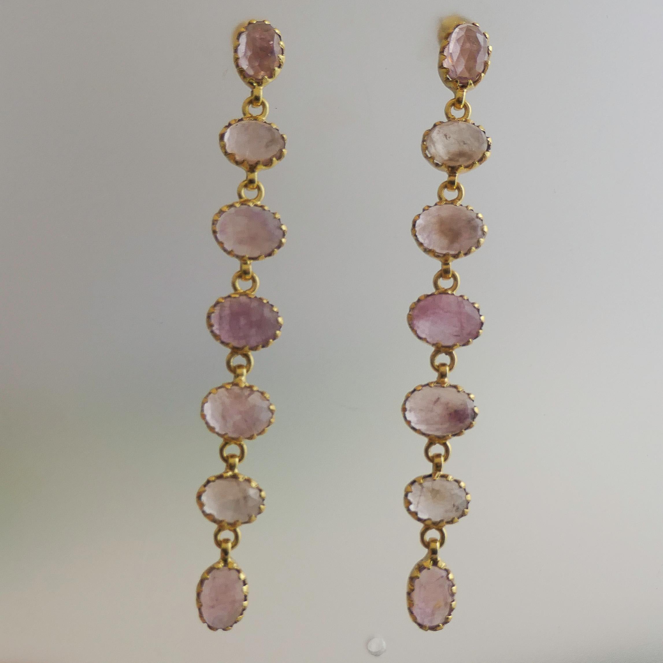 Ces gracieuses boucles d'oreilles longues présentent une série de neuf saphirs roses ovales à facettes de 8x6 mm, chacun délicatement serti dans de l'argent sterling plaqué or avec une monture à griffes raffinée. Les pierres précieuses se déclinent