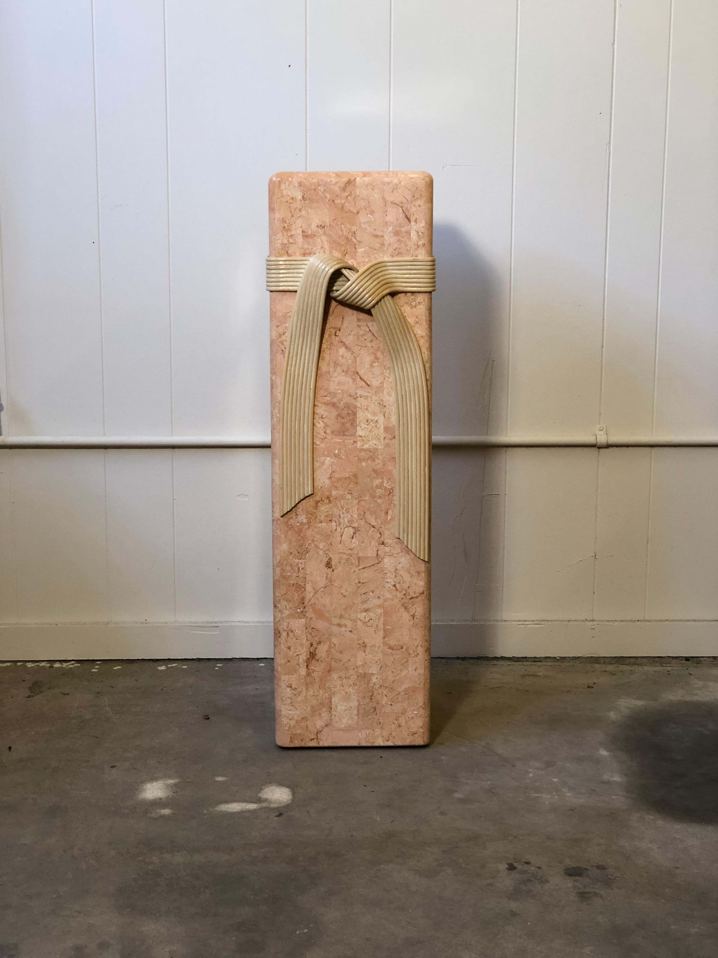 Late 20th century Hollywood Regency style square pedestal base of pink tessellated stone with an exaggerated ribbon tie of rattan.