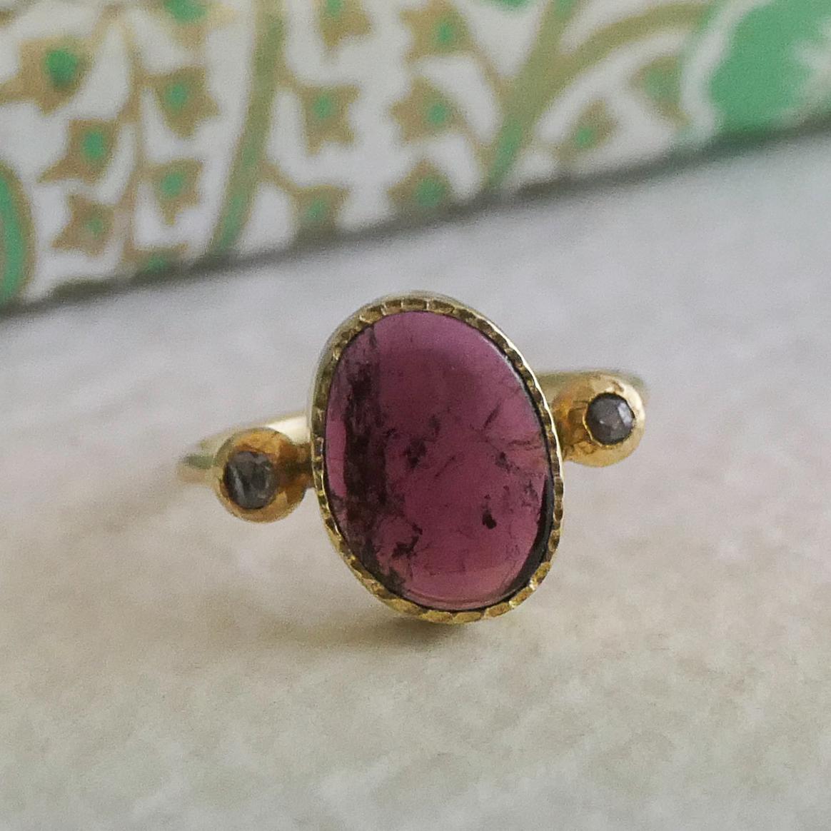 Dieser elegante Ring zeigt einen 7x10 mm großen rosafarbenen Turmalin-Cabochon in freier Form, eingefasst in vergoldetes Sterlingsilber. Seine organische Form und der kräftige Beerenton machen ihn zu einem echten Hingucker. Zwei 1,7 mm große braune