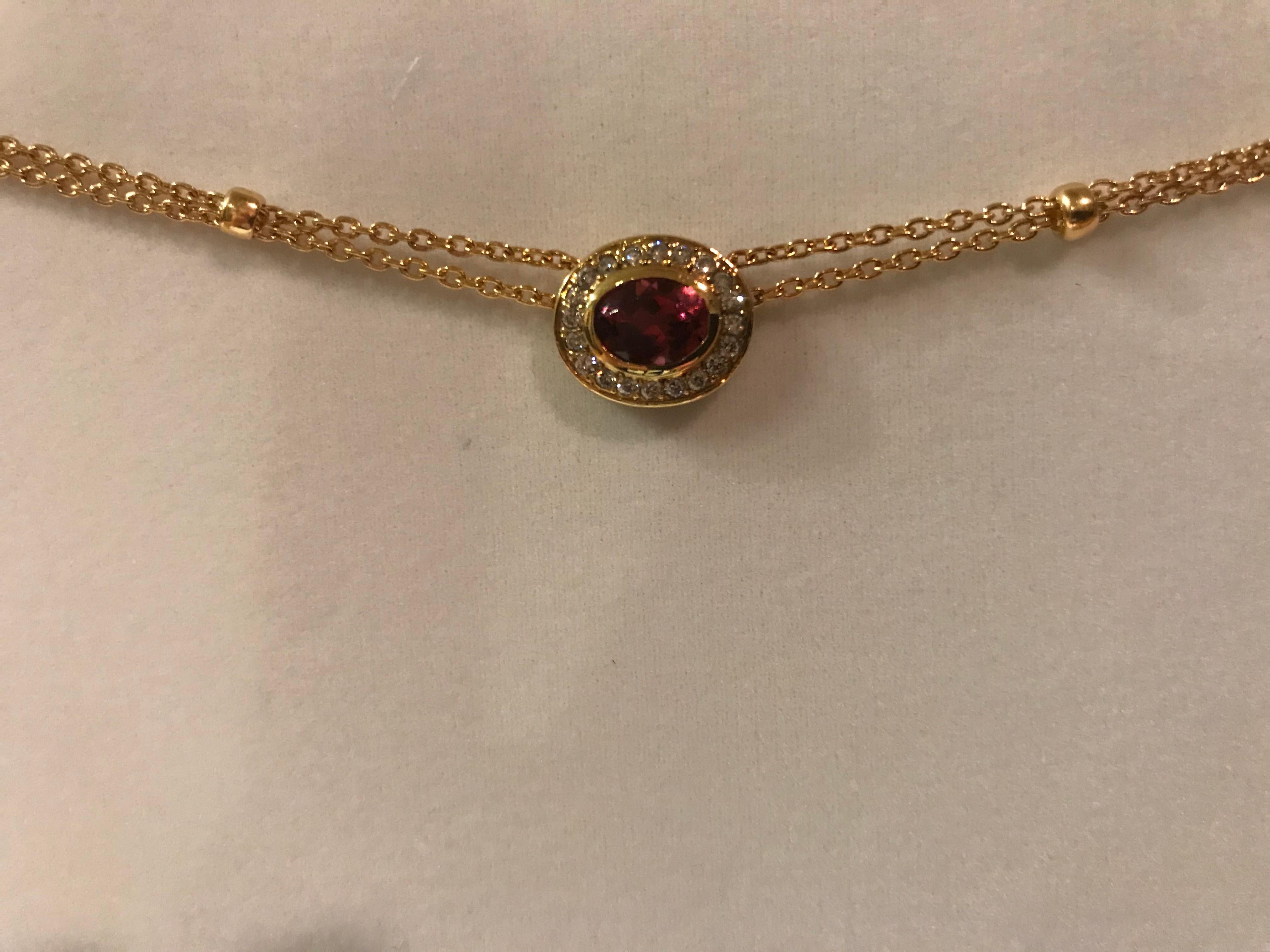 18K yellow gold necklace containing one bezel set oval faceted tourmaline weighing 1.33 carats surrounded by a halo containing diamonds weighing combined 0.28 carat. The necklace is a double strand chain with gold beads.