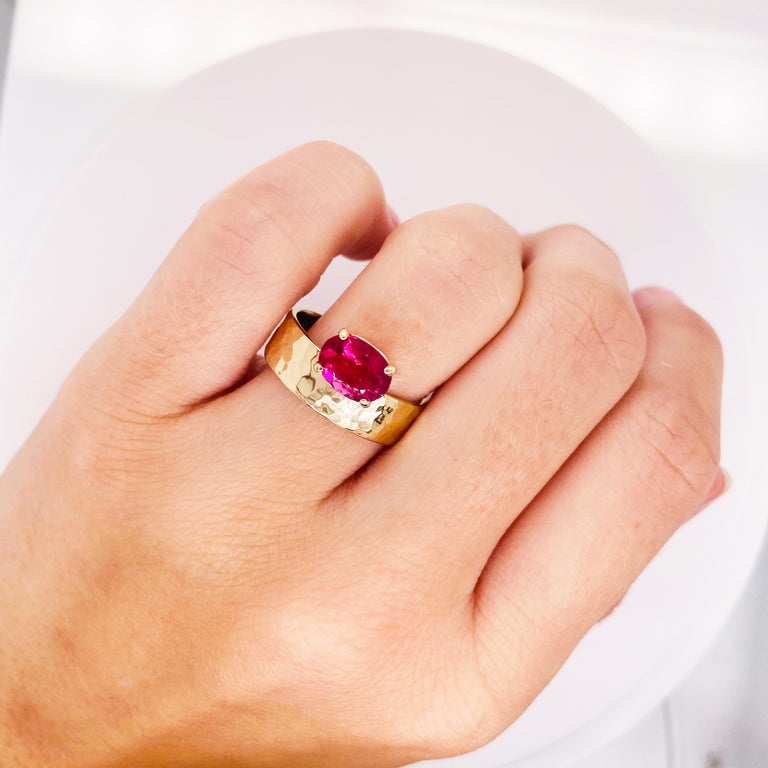 This asymmetrical 14 karat yellow gold hammered ring has a gorgeous magenta pink tourmaline in the front and center! The gemstone weighs 1.32 carats and is set in a strong basket setting of 14 karat gold. The band is 6 millimeters(mm) wide and the