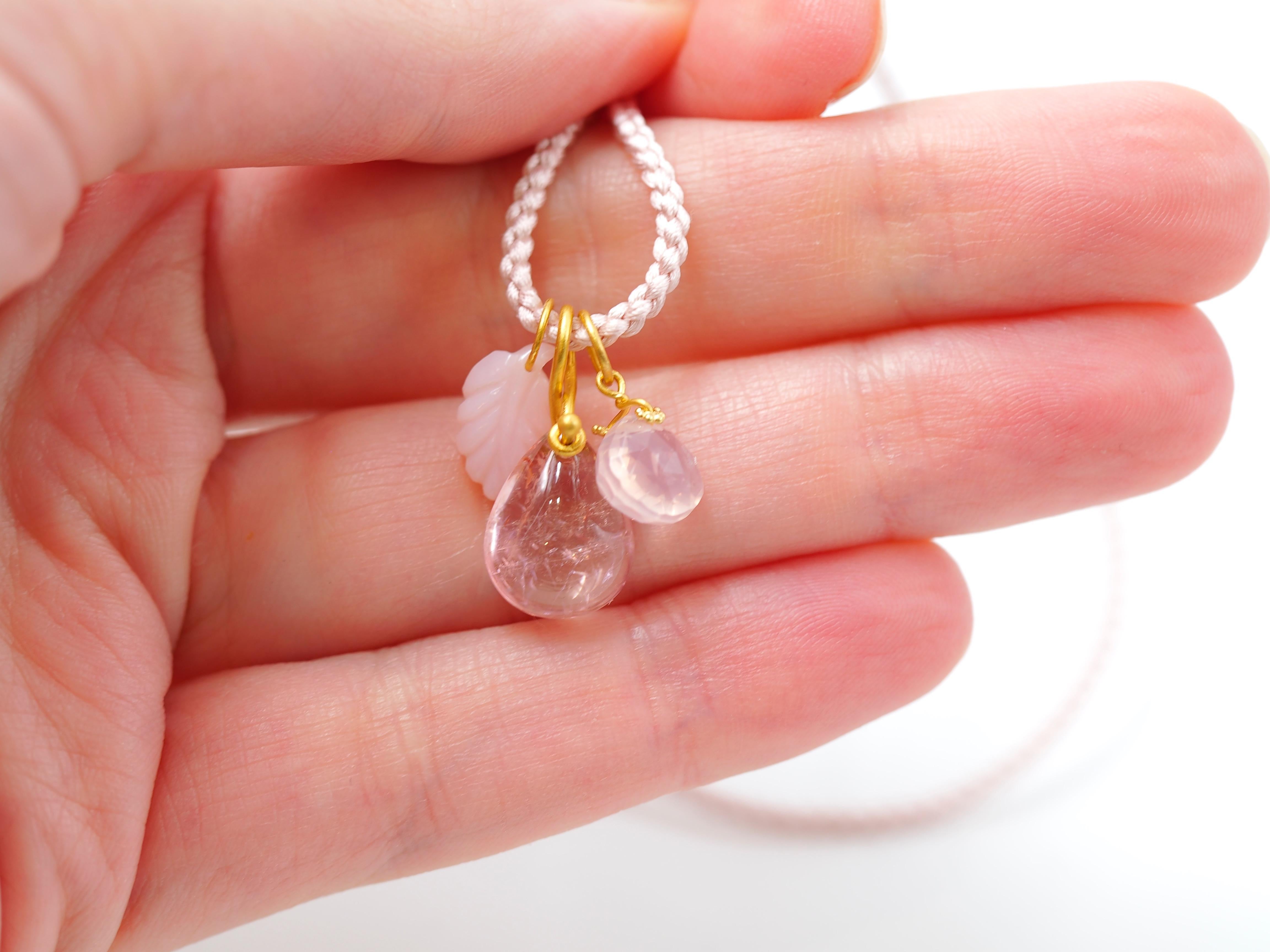 This delicate necklace is composed of 3 pendants on a long braided silk rope:
- a light pink tourmaline cabochon simply drilled with a twisted gold ring
- a small faceted tabi in rose quartz with a twisted gold ring
- a pink opal leaf
All stones