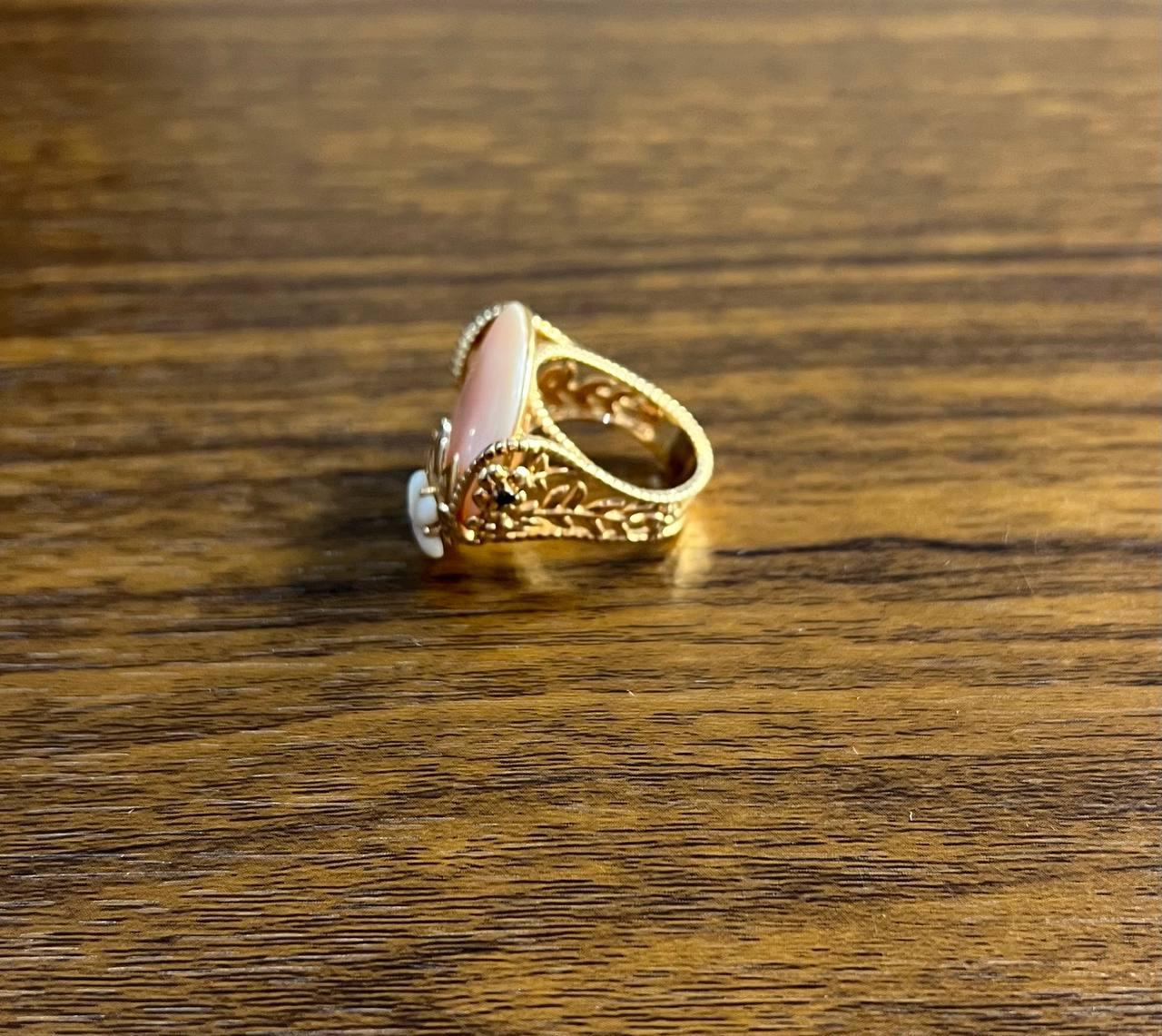 A statement ring featuring a large pink white mother of pearl with a smooth, rounded surface.

The ring is adorned with intricate gold detailing, including a floral MOP motif with delicate petals and leaves. In 14K Rose Gold.