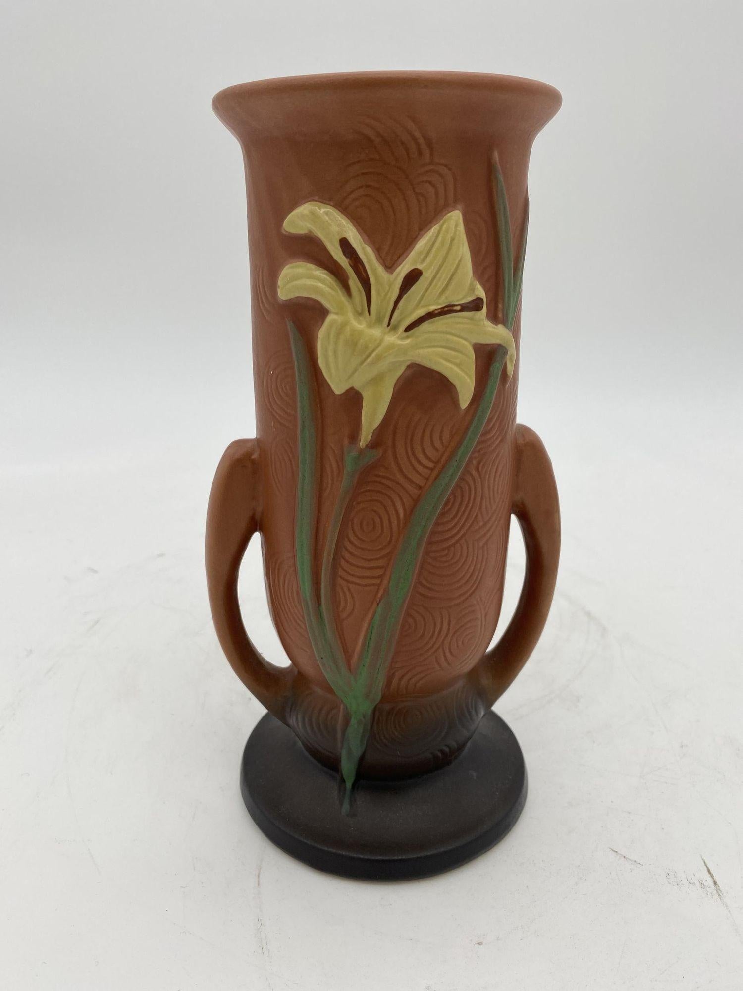 Vintage 1946 Art Nouveau Zephyr Lily brown art pottery flower vase by Roseville number 133-8. The vase features a flute shape and has a relief of a yellow lily with a black base that fades into brown and gradually fades into pinkish salmon