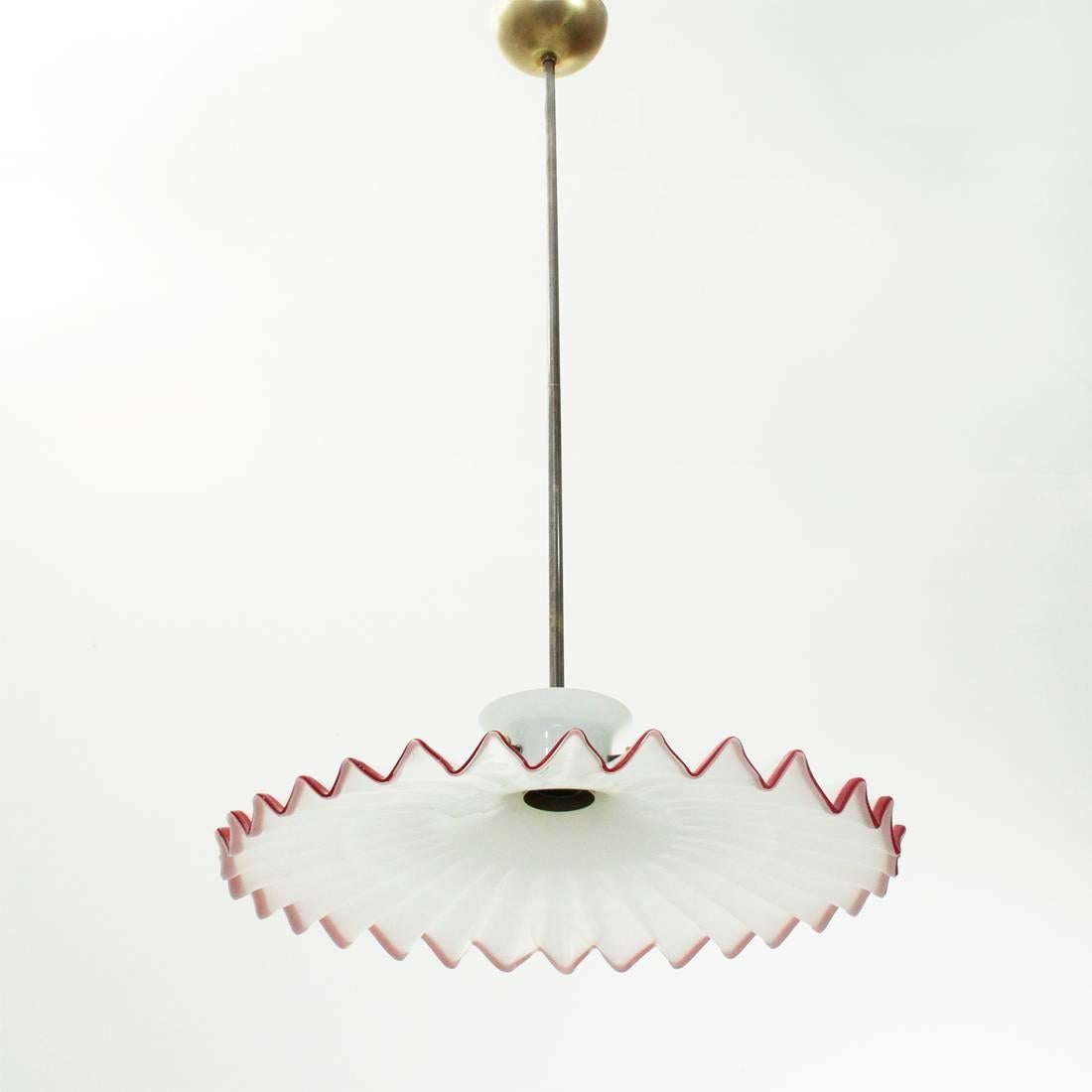 Araña fabricada por Venini en los años setenta sobre un proyecto de Ludovico Diaz de Santillana.
Roseta, vástago, portalámparas y tornillos, de latón bruñido.
Difusor de cristal blanco con borde rojo.
Buenas condiciones generales, roseta con