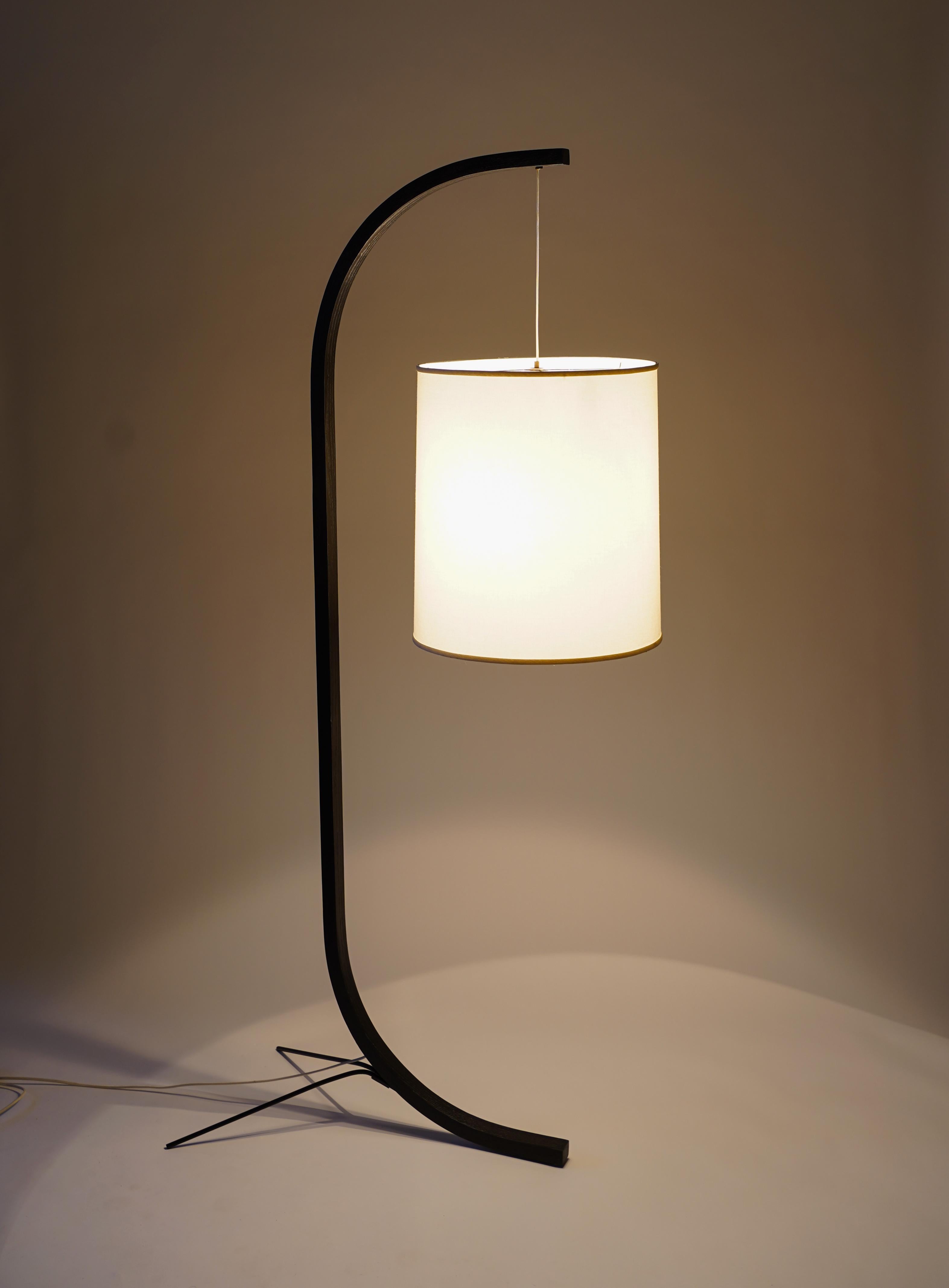 Slender Minimalist curved floor lamp made with oak, steel, and cloth lampshade. Powered by a traditional incandescent bulb, the lamp provides a 360° warm glow. This version of the Pion lamp is offered in a black finish. The lamp can receive two