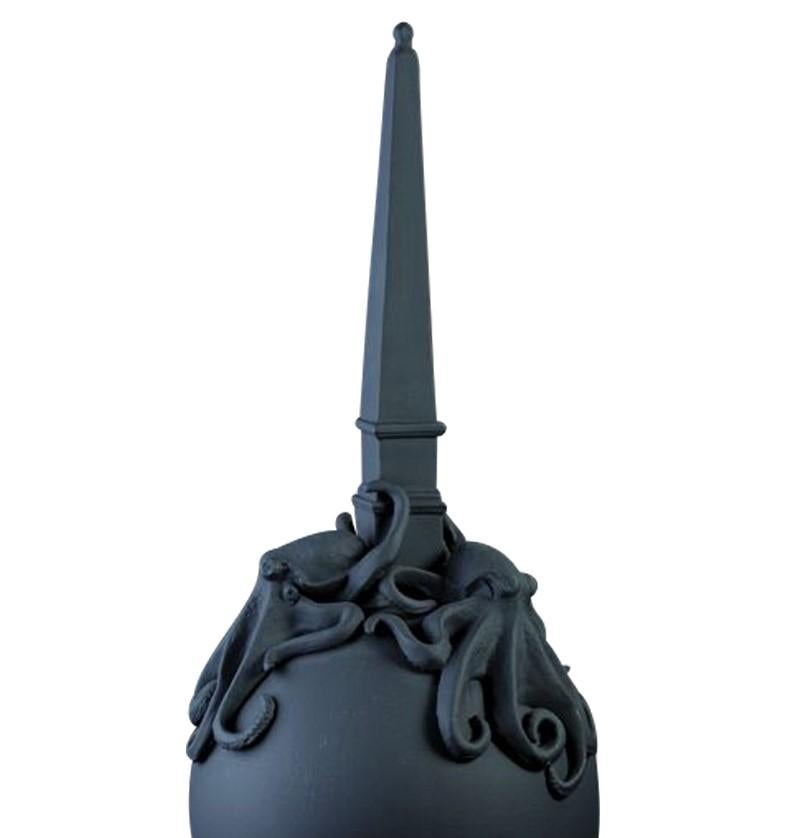 This striking decorative piece, entirely finished with a matte black polish, features a globe standing on a small pedestal and supporting an obelisk on whose base two magnificent octopi seem to be moving their tentacles, reproduced in all their