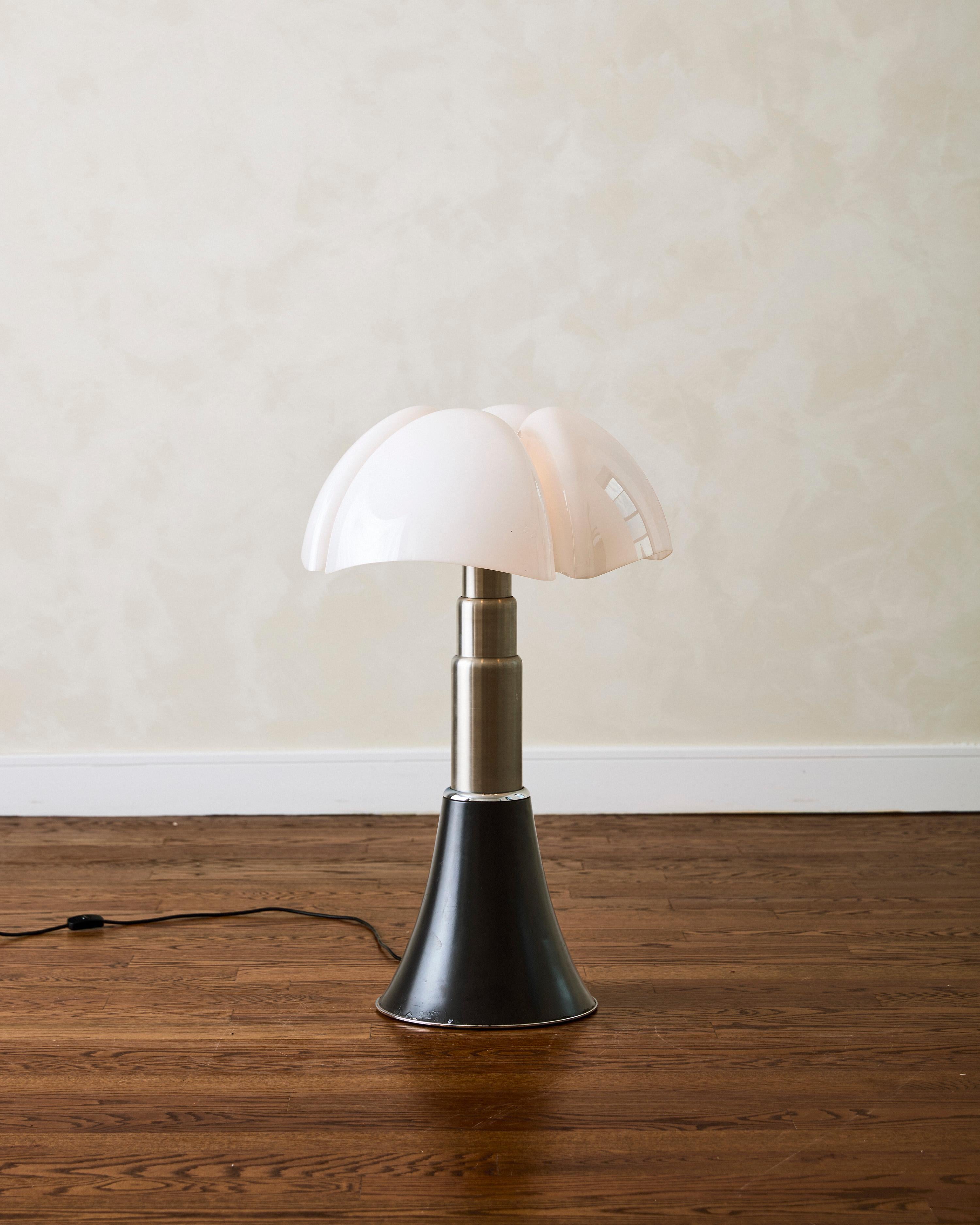 The Pipistrelle table lamp by Gae Aulenti for Martinelli Luce features a white opal methacrylate diffuser and a base made of glossy black-coated aluminum with a satin aluminum trim. Designed for use as both a table and standing lamp, it provides