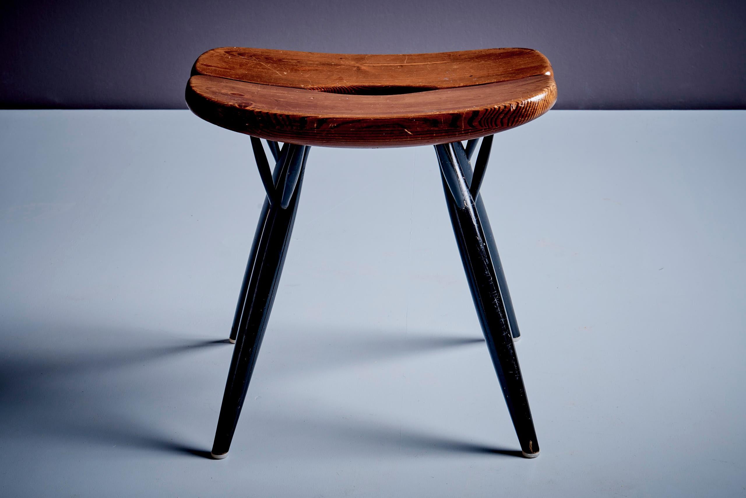 Pirkka stool by Ilmari Tapiovaara for Laukaan Puu. Features a sculpted pine seat with signature central split and black lacquered birch legs. Branded stamps on the underside confirm authenticity. A classic of Finnish mid-century design with