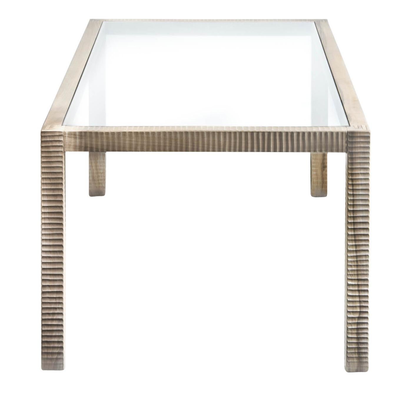 This elegant table is entirely made in Italian walnut wood. The structure features interlocking pieces of wood with visible points and pins and the geometric pattern of the surfaces is hand-carved with a plane. The top glass is nestled in the
