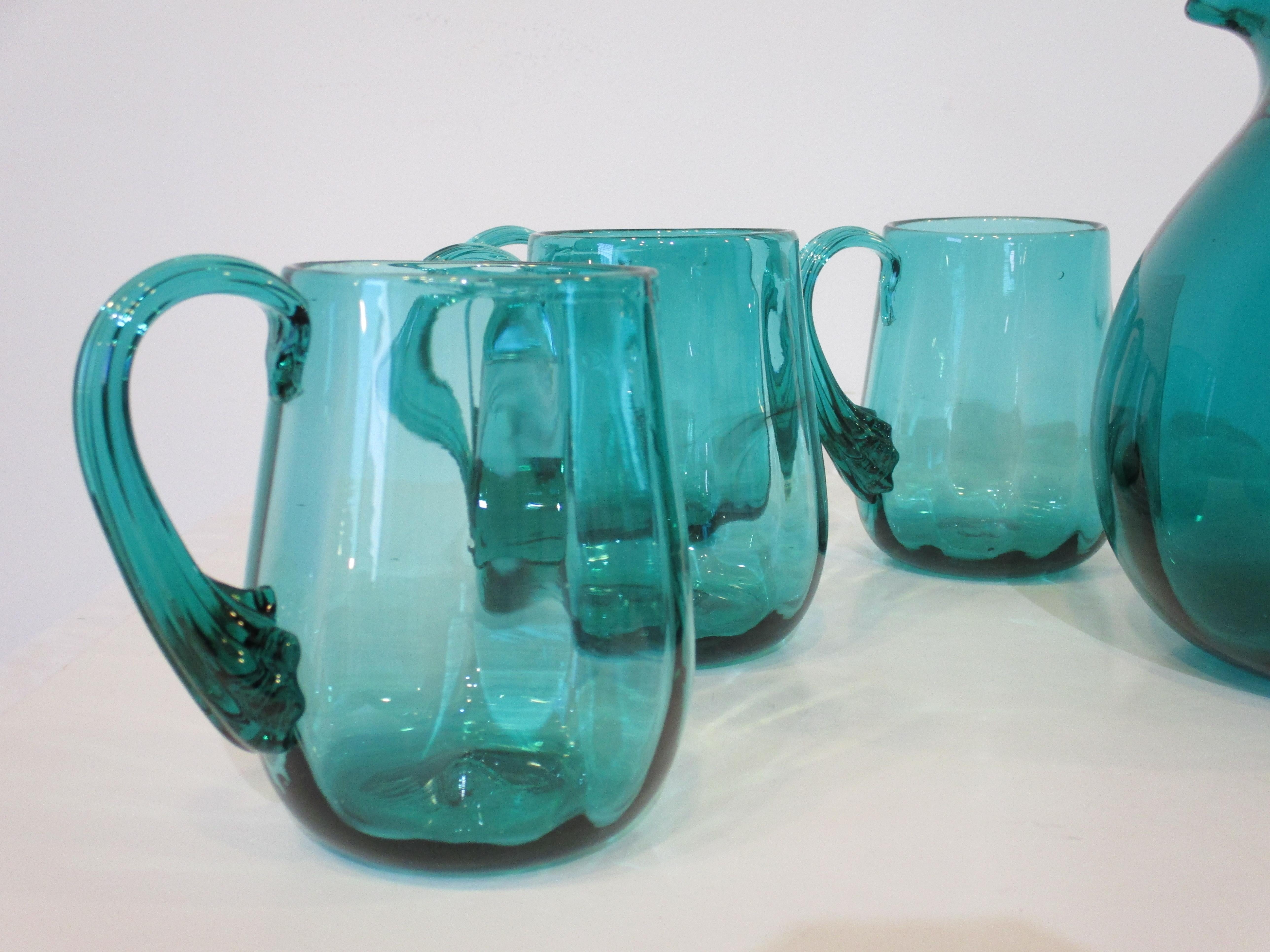 A nine piece handblown pitcher and mug set in a sea green color by noted glass artist Wayne Husted who's iconic pieces defined the Mid Century period . The mugs and pitcher have nice flowing handles with line detail perfect for that summer night