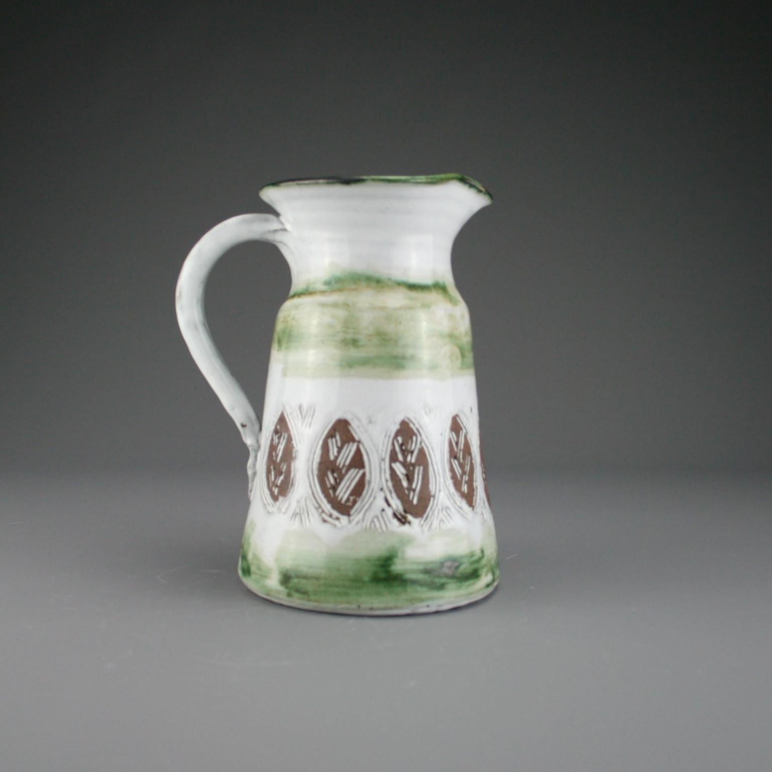 A charming and rustic French midcentury decorative pitcher by Albert and Pyot Thiry, circa 1960s. A soft green glaze encircles the exterior of the pitcher which is decorated with an incised repeating floral motif exposing the brown clay underneath.