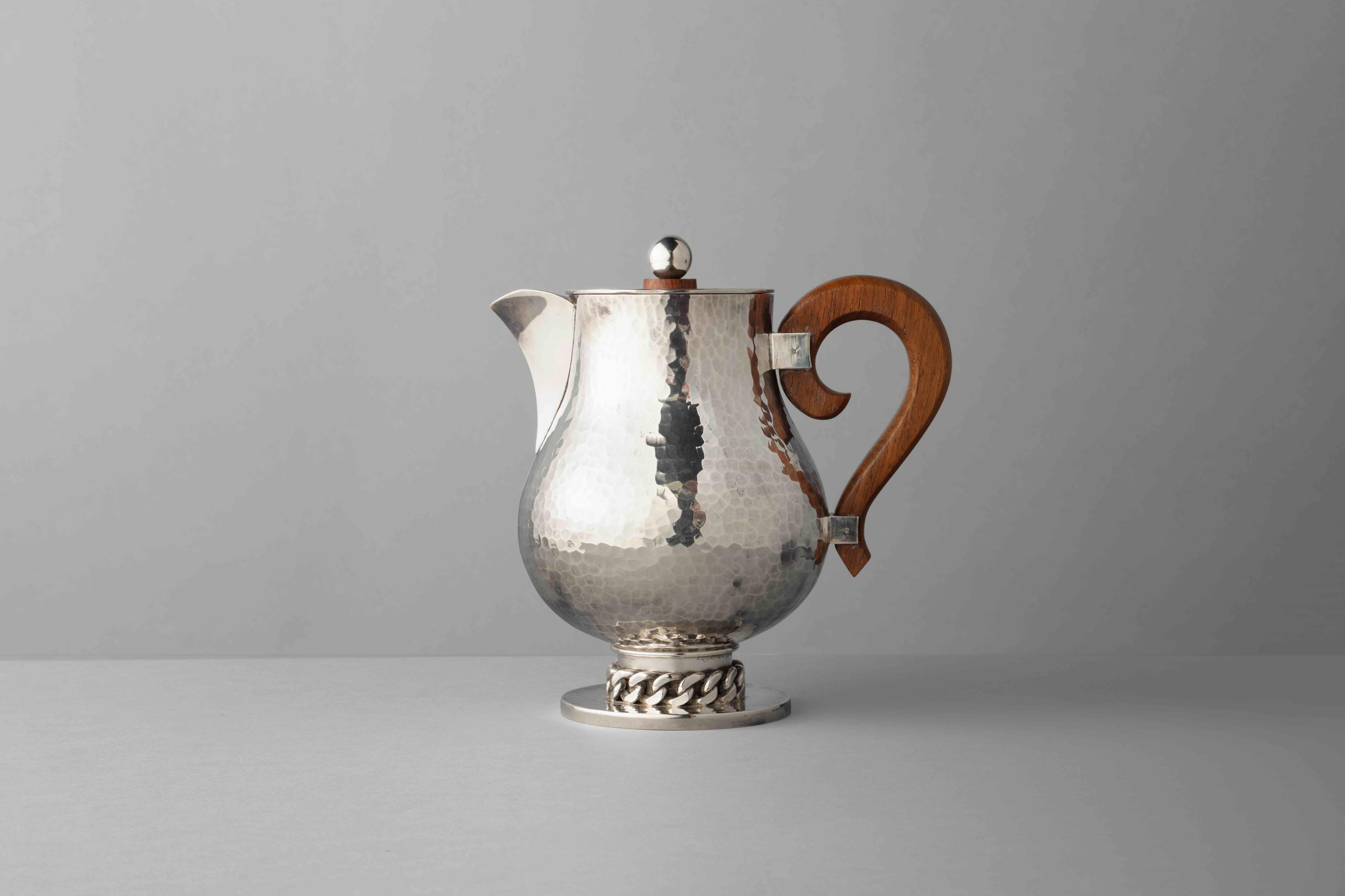 Heavy gauge silver plated pitcher in a hammered finish with Despres’ Signature chain motif around the base and a wooden handle.
  