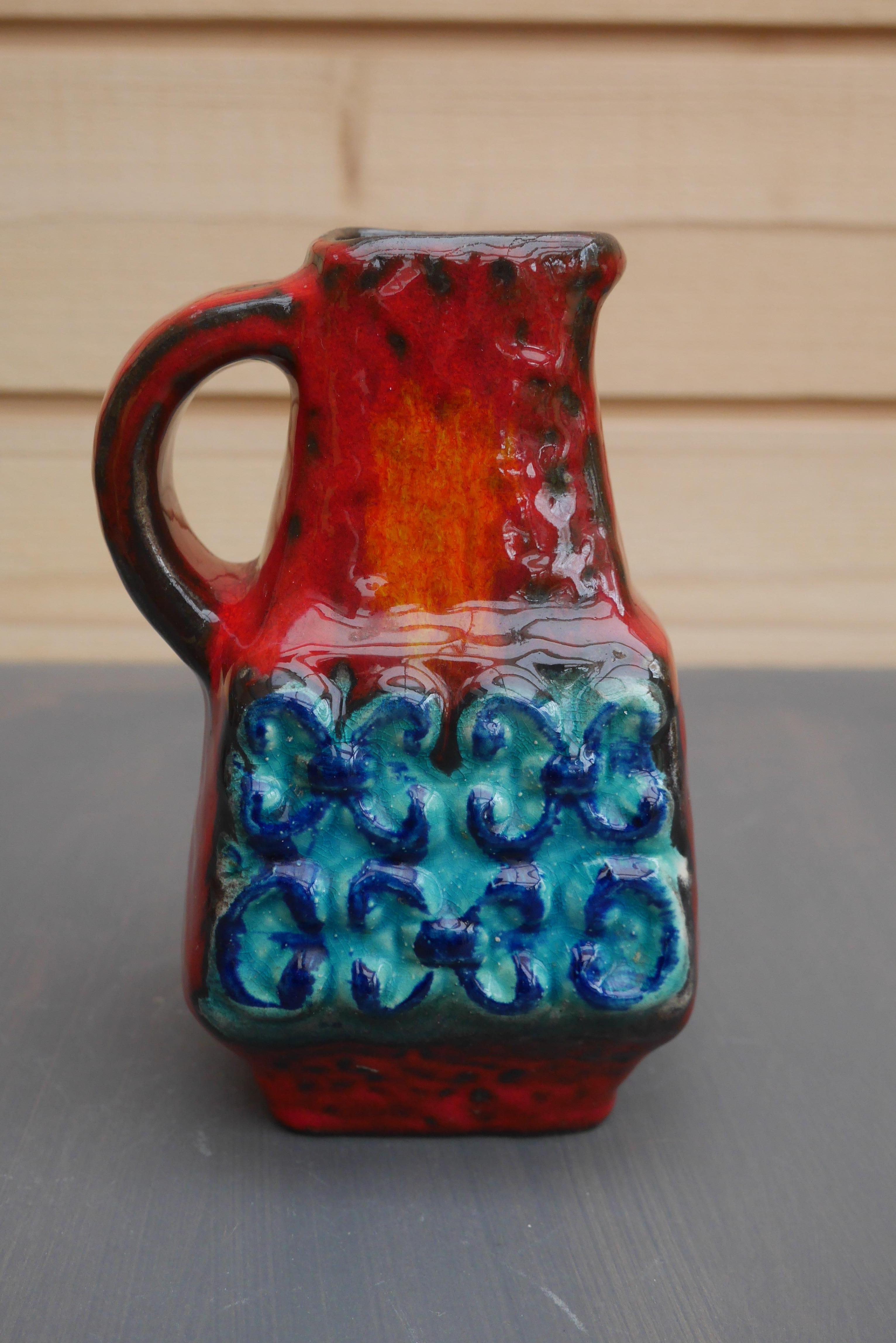 Fantastic small pitcher or vase from Bay Ceramics, West Germany. Very colorful orange and red glazing with turquoise highlights on the textured lower part. Marked with the model number 254/17.
Bay Keramik fabrik was founded by Eduard Bay in 1933 in