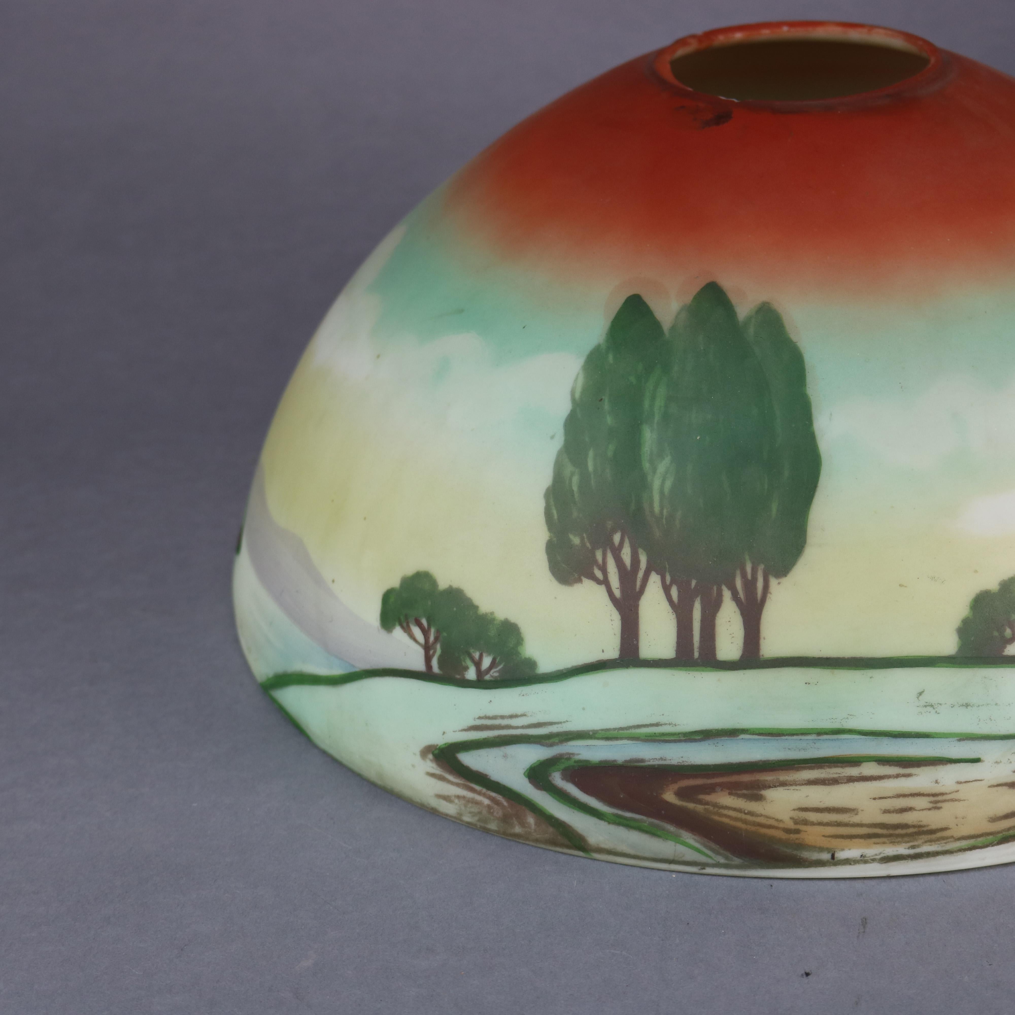 An antique Arts & Crafts table lamp in the manner of Pittsburgh Lamp Co. offers cast double socket base having embossed stylized foliate collar surmounted by dome glass shade having obverse hand painted landscape scene with river or lake and trees,